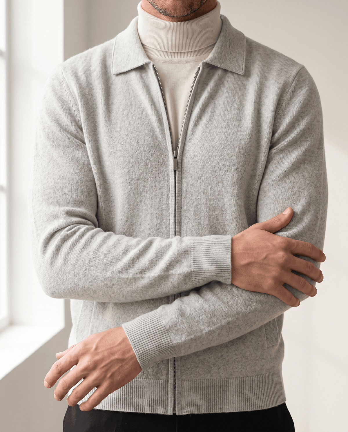 Arms crossed in a light gray zip cardigan layered over a cream turtleneck