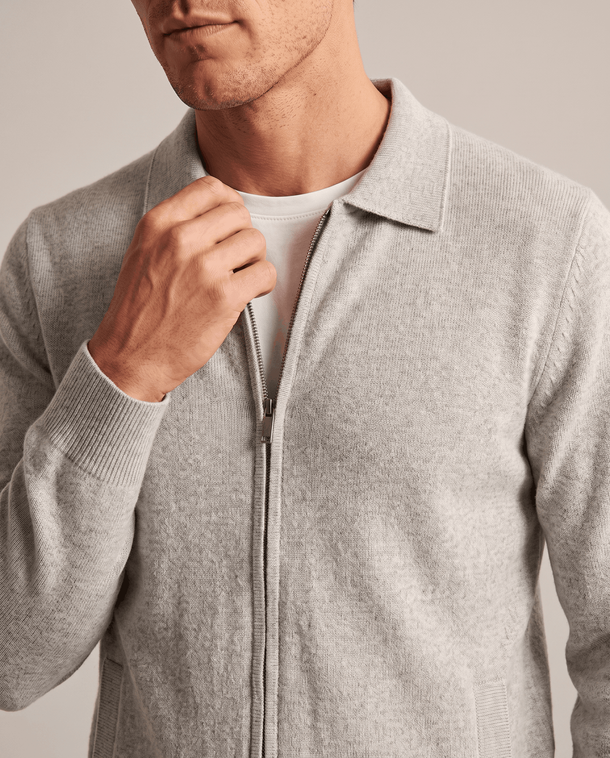 Hand at the zip of a light gray knit cardigan worn over a white tee