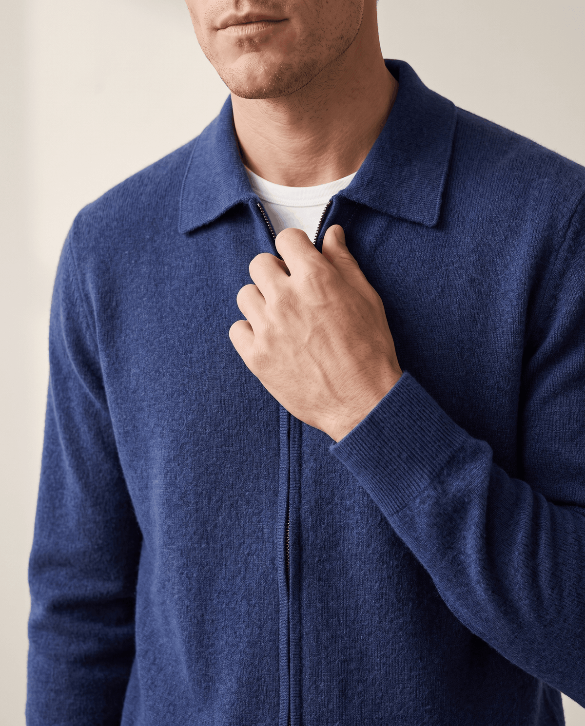 Hand at the zip of a navy textured knit cardigan over a white tee