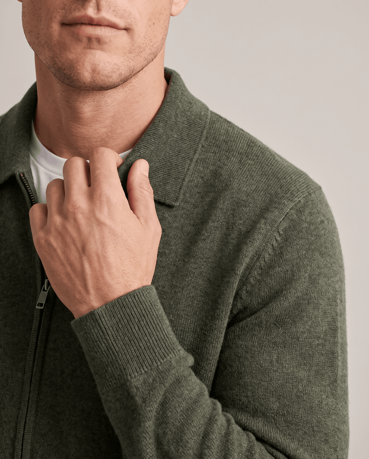 Hand at the collar of an olive green knit cardigan over a white tee