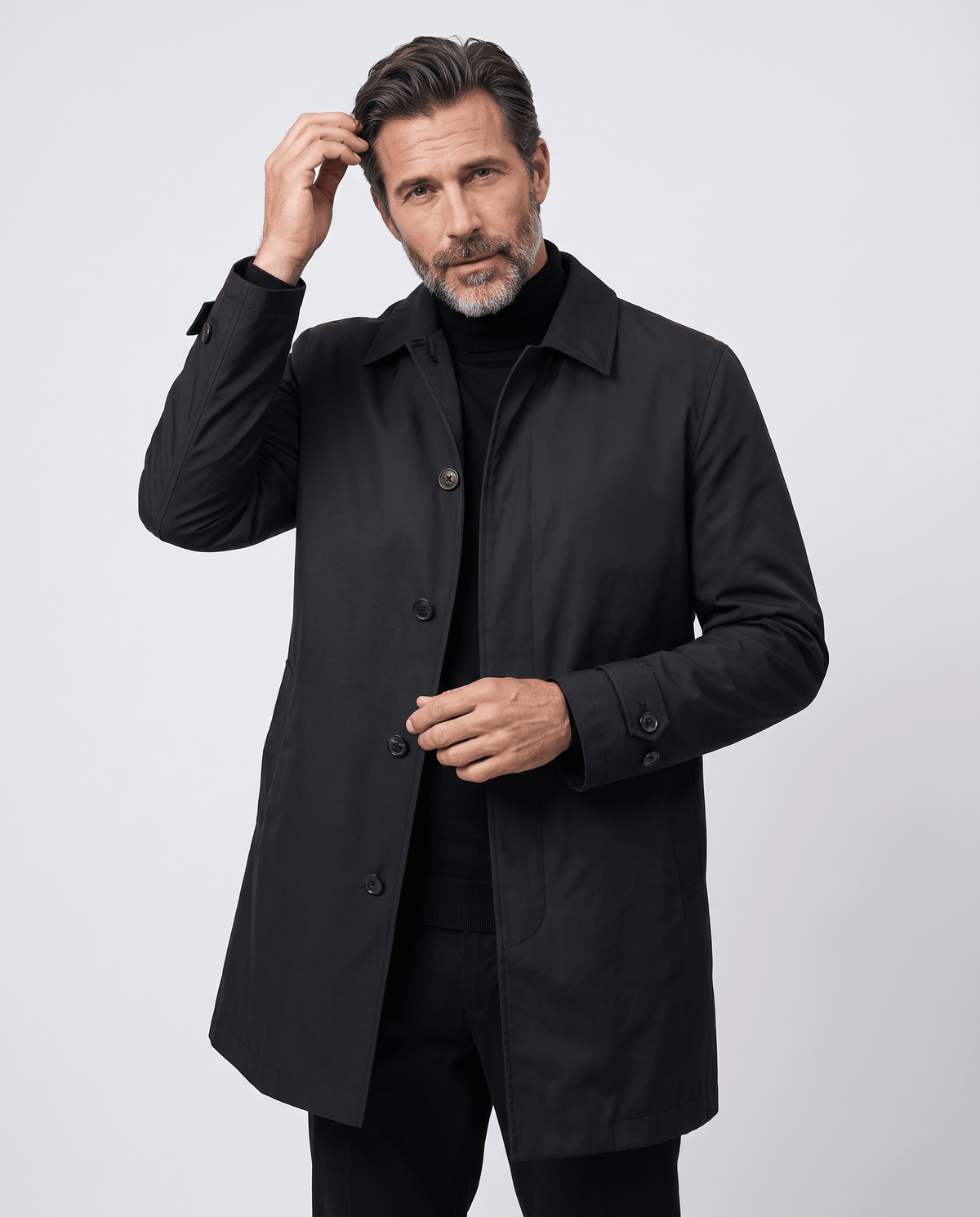 Black trench coat worn open with one hand holding the collar