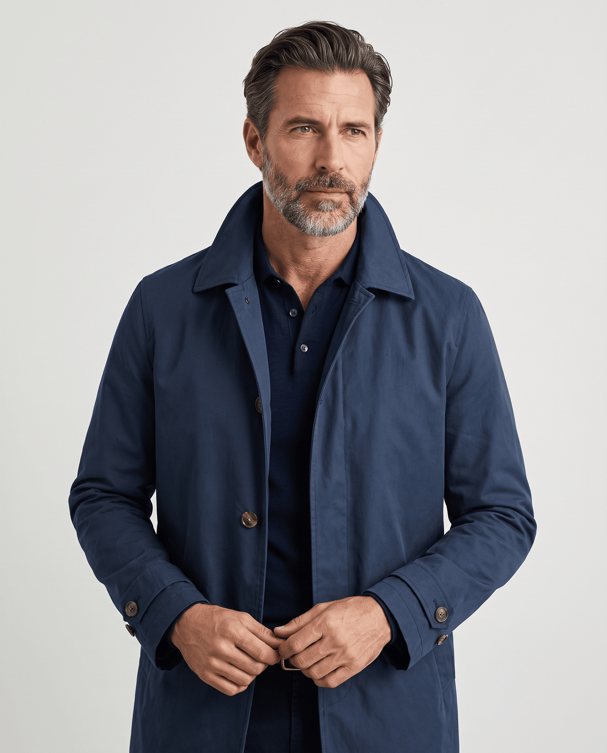 Navy blue trench coat worn over a black roll-neck with hands at the front