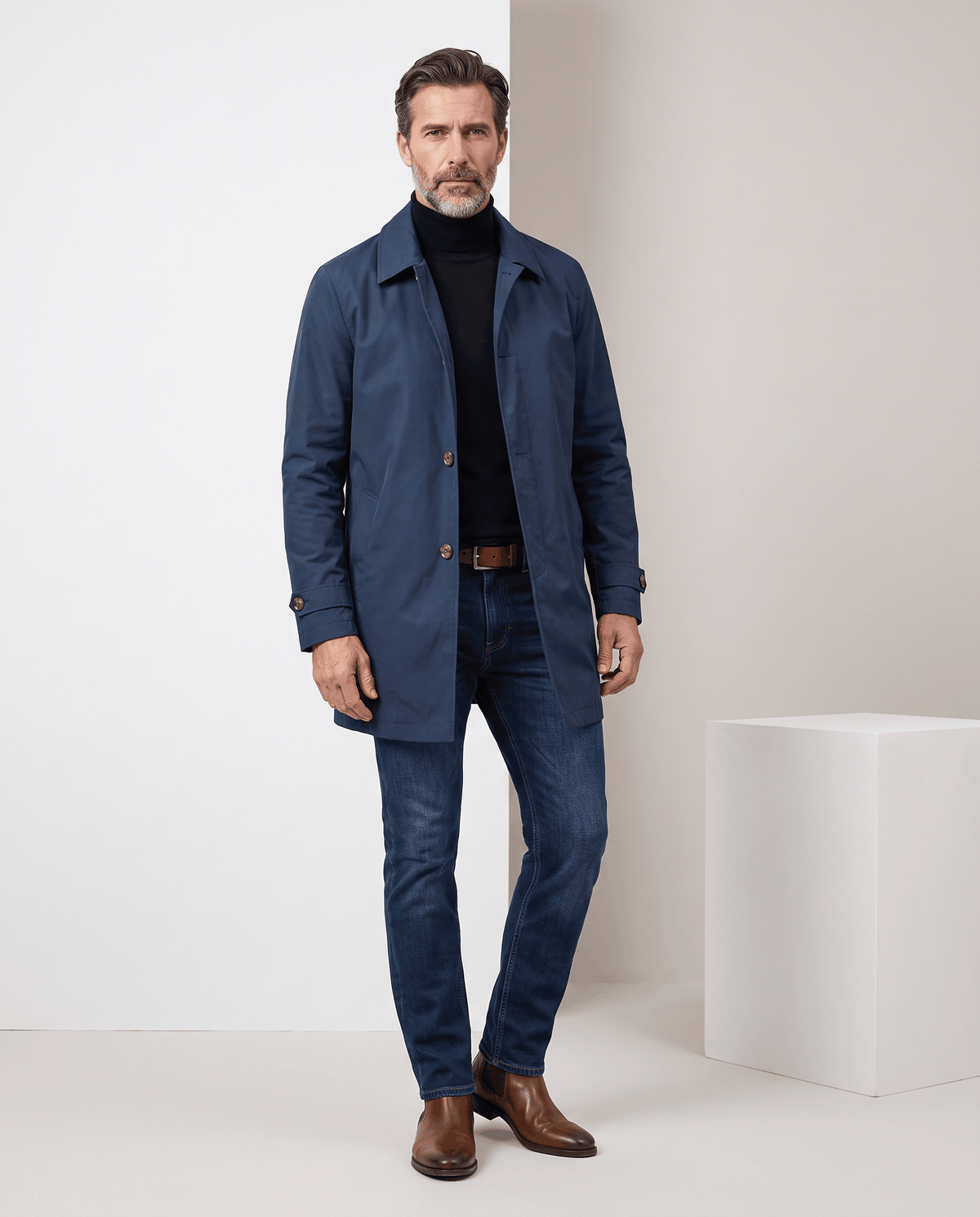 Full-length navy blue trench coat styled with blue jeans and brown shoes