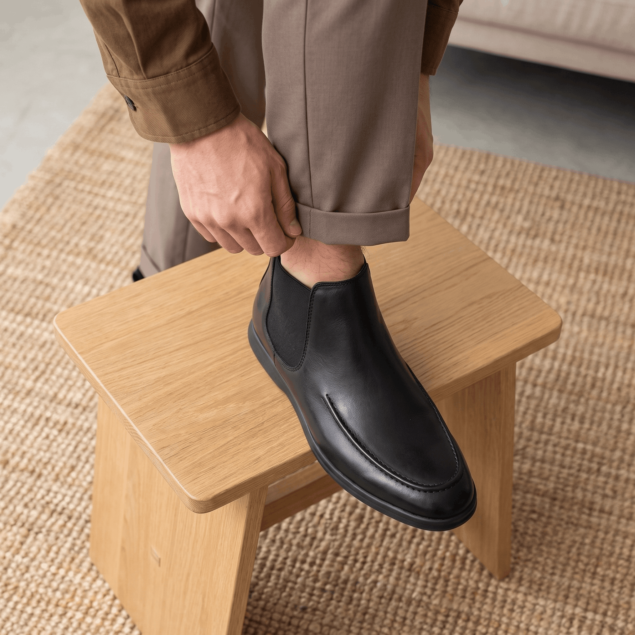 Person wearing black moc toe Chelsea boots while seated on a wooden stool, showing the slim cupsole and low profile.