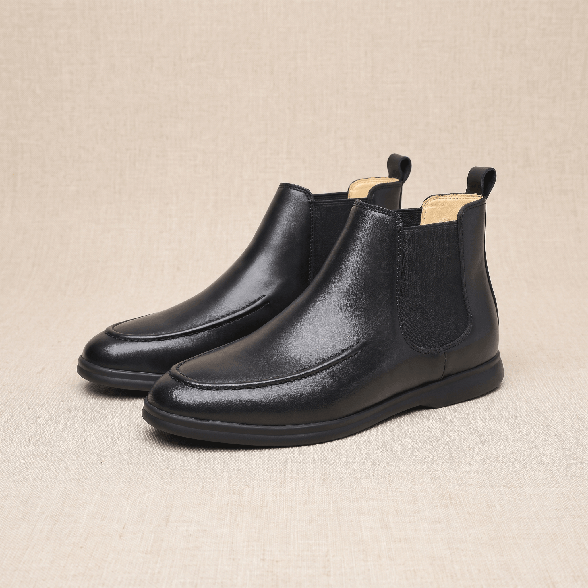 Pair of black smooth-grain moc toe Chelsea boots with elastic side panels, pull tabs, and slim cupsoles.