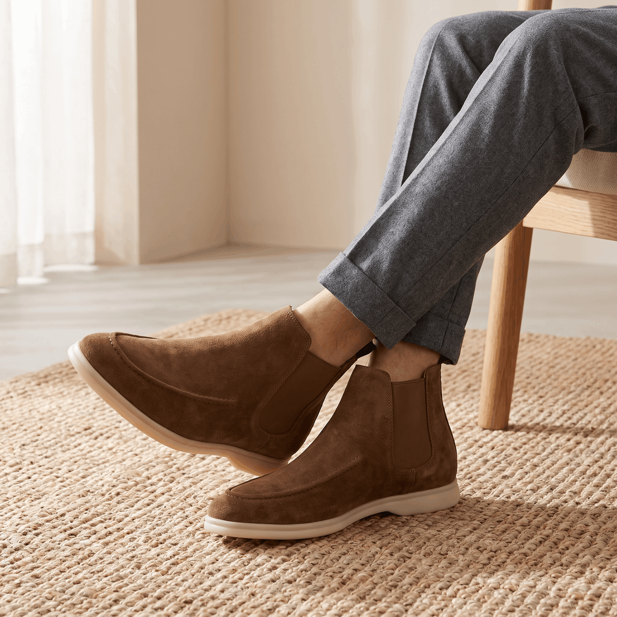 Person wearing brown suede moc toe Chelsea boots with grey trousers, showing the side profile and low sole.