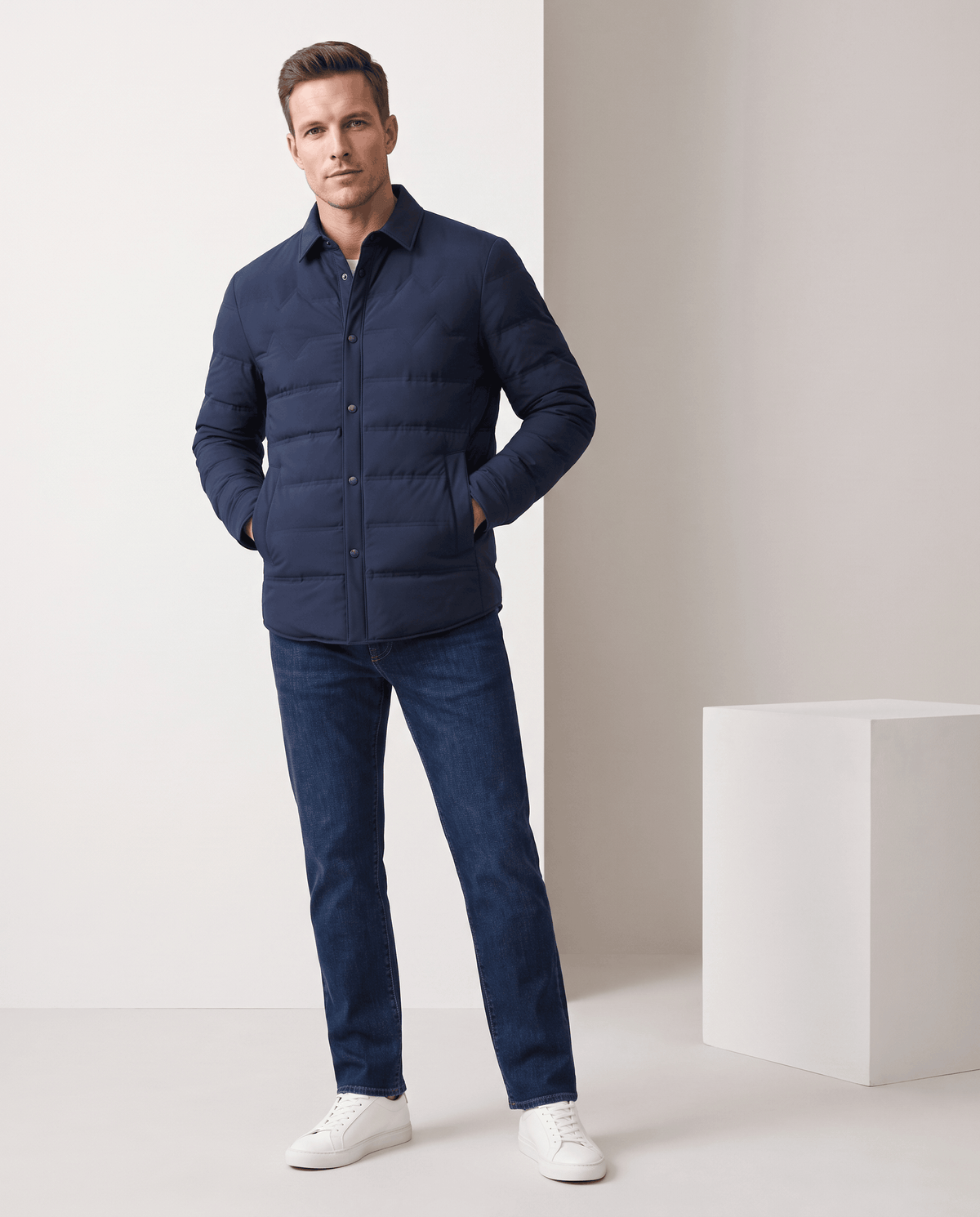 Man standing in a navy quilted puffer jacket with blue jeans, full-length view