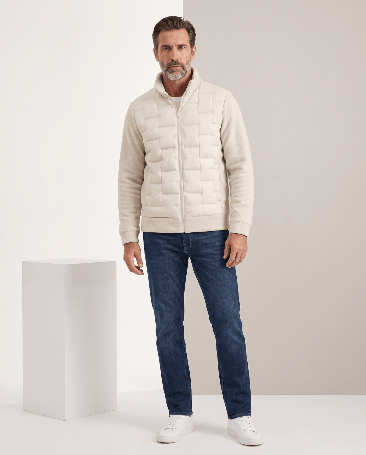 Man standing in an off-white hybrid puffer jacket with blue jeans, full-length view