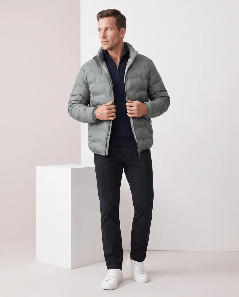 Man standing in an olive green quilted puffer jacket with a white tee and dark trousers