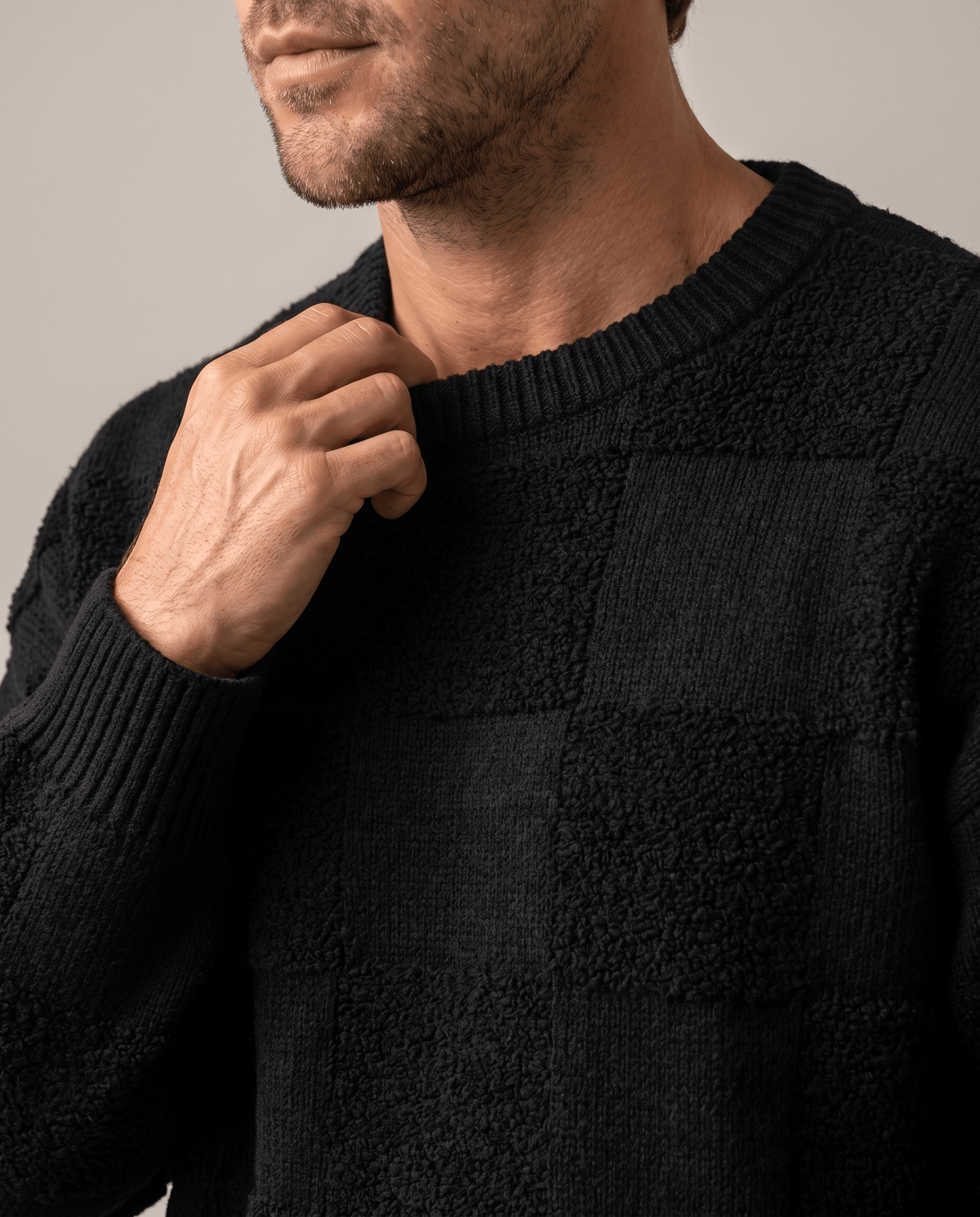 Close-up of hand at the ribbed crew collar of a black textured knit