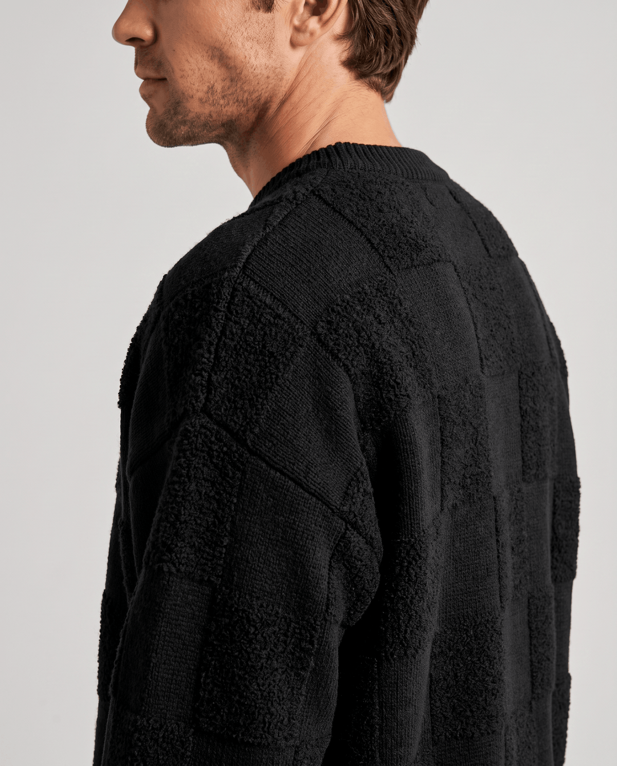 Side close-up of black sweater shoulder showing tonal grid texture