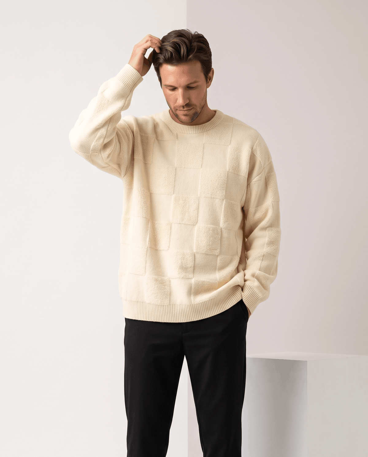 Model in cream oversized knit sweater with black trousers, hand in hair