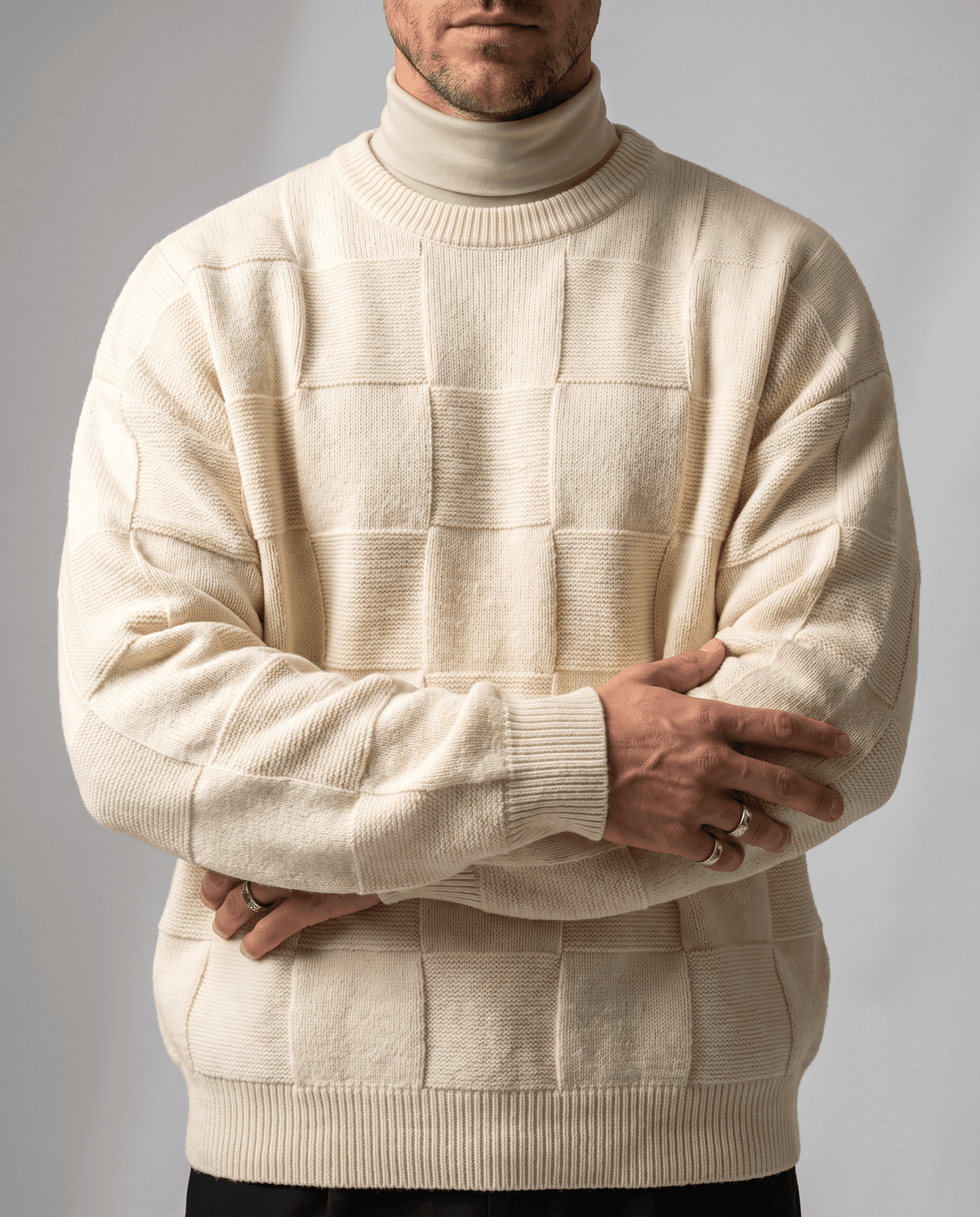 Cream checkerboard knit over a matching turtleneck with arms folded