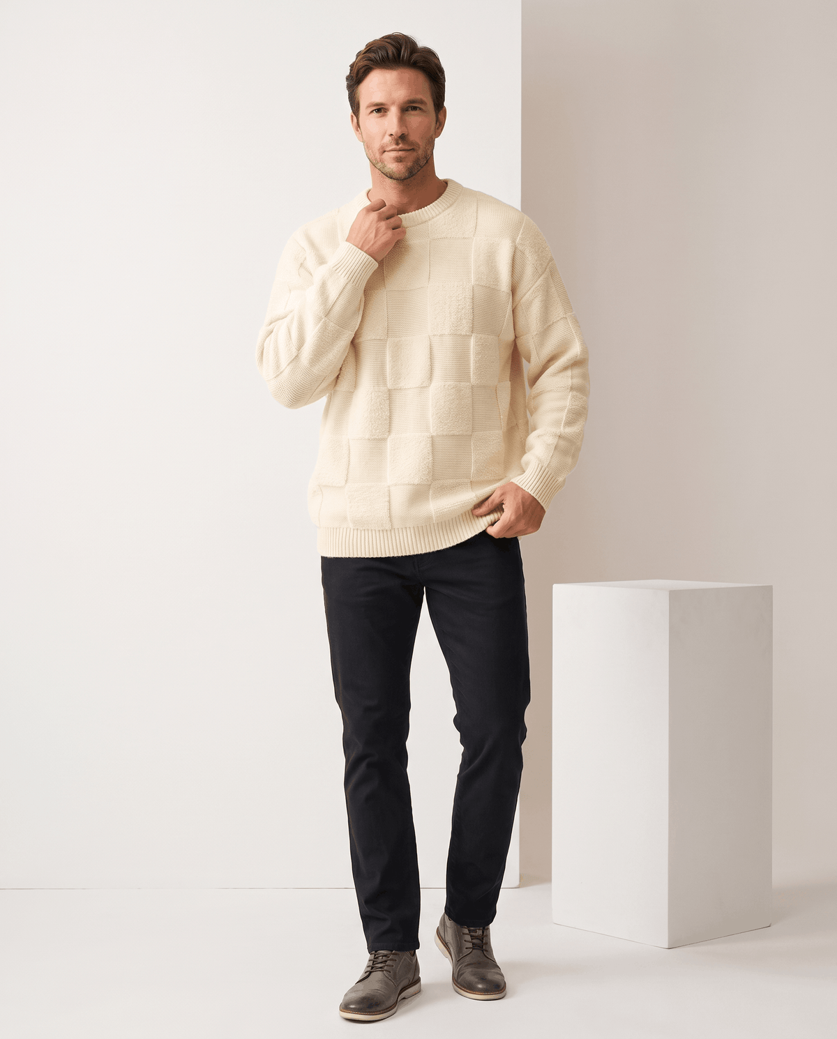 Full-length cream checkerboard sweater outfit with black jeans and boots