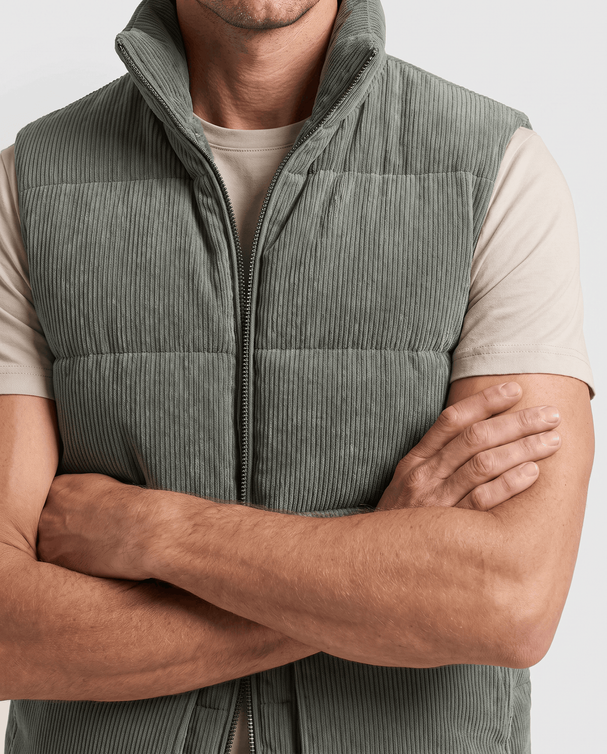 Close-up of green corduroy vest front with quilted pattern, arms crossed over a cream shirt