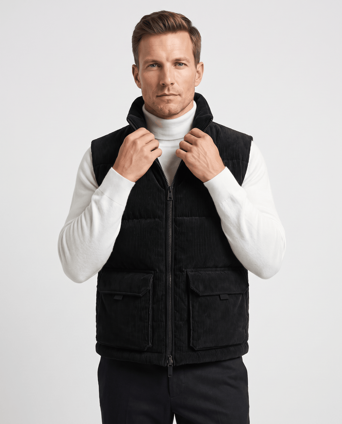 Black corduroy vest zipped to the collar over a white turtleneck, flap pockets visible