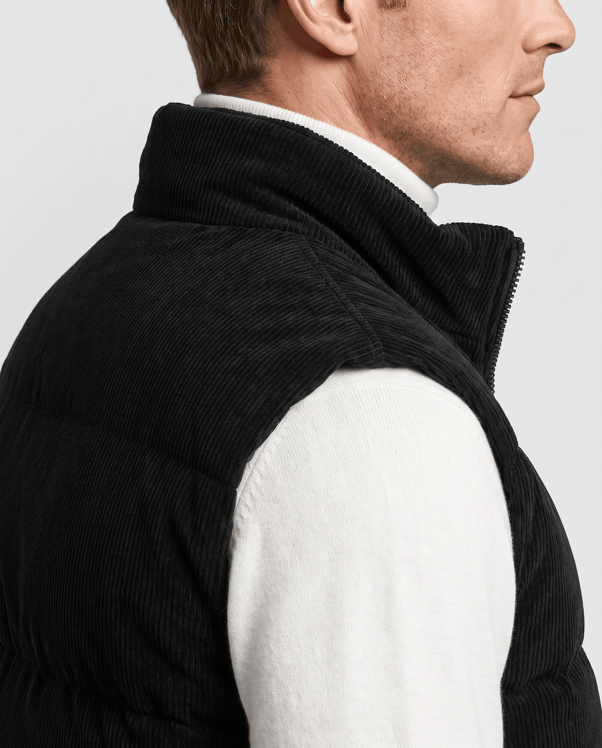 Side close-up of black corduroy vest showing the stand collar over a white sweater