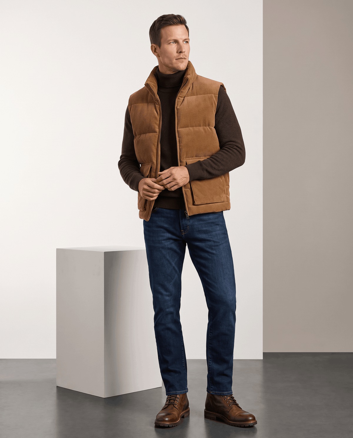 Man in brown corduroy vest over a dark brown sweater with jeans and shoes in studio