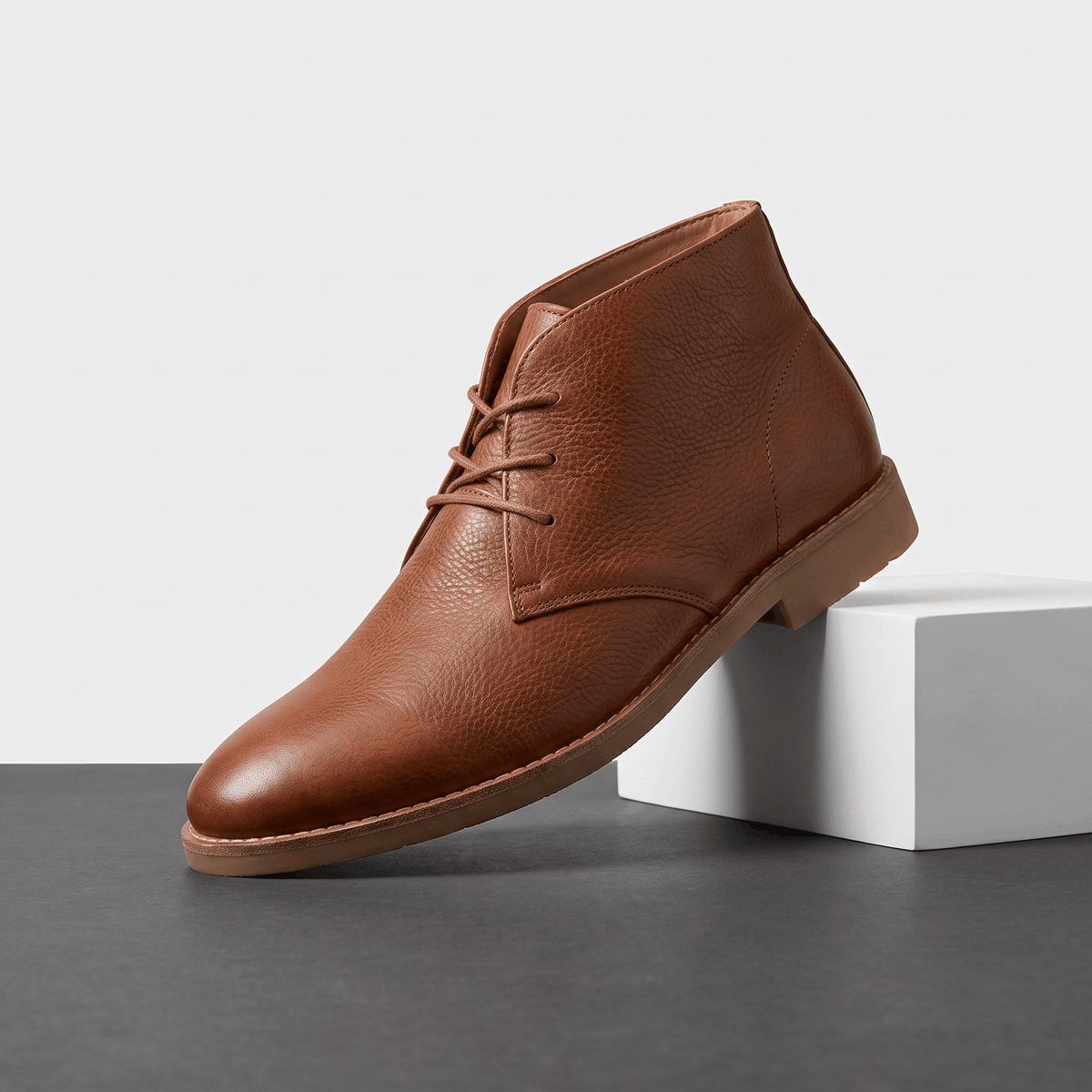 Light brown leather lace-up ankle boot displayed on a white pedestal.