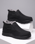 Black fleece-lined slip-on ankle boots with rugged rubber soles displayed on white blocks.