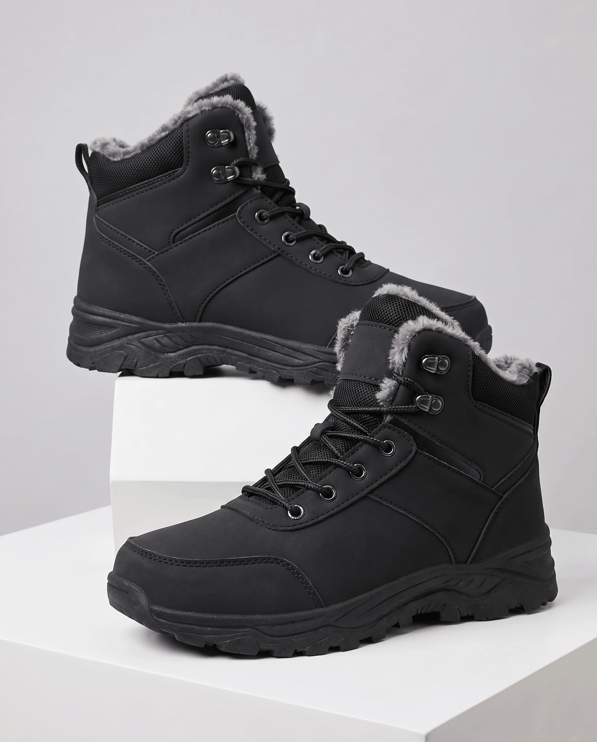 Black insulated lace-up winter boots with rugged soles displayed on white blocks.