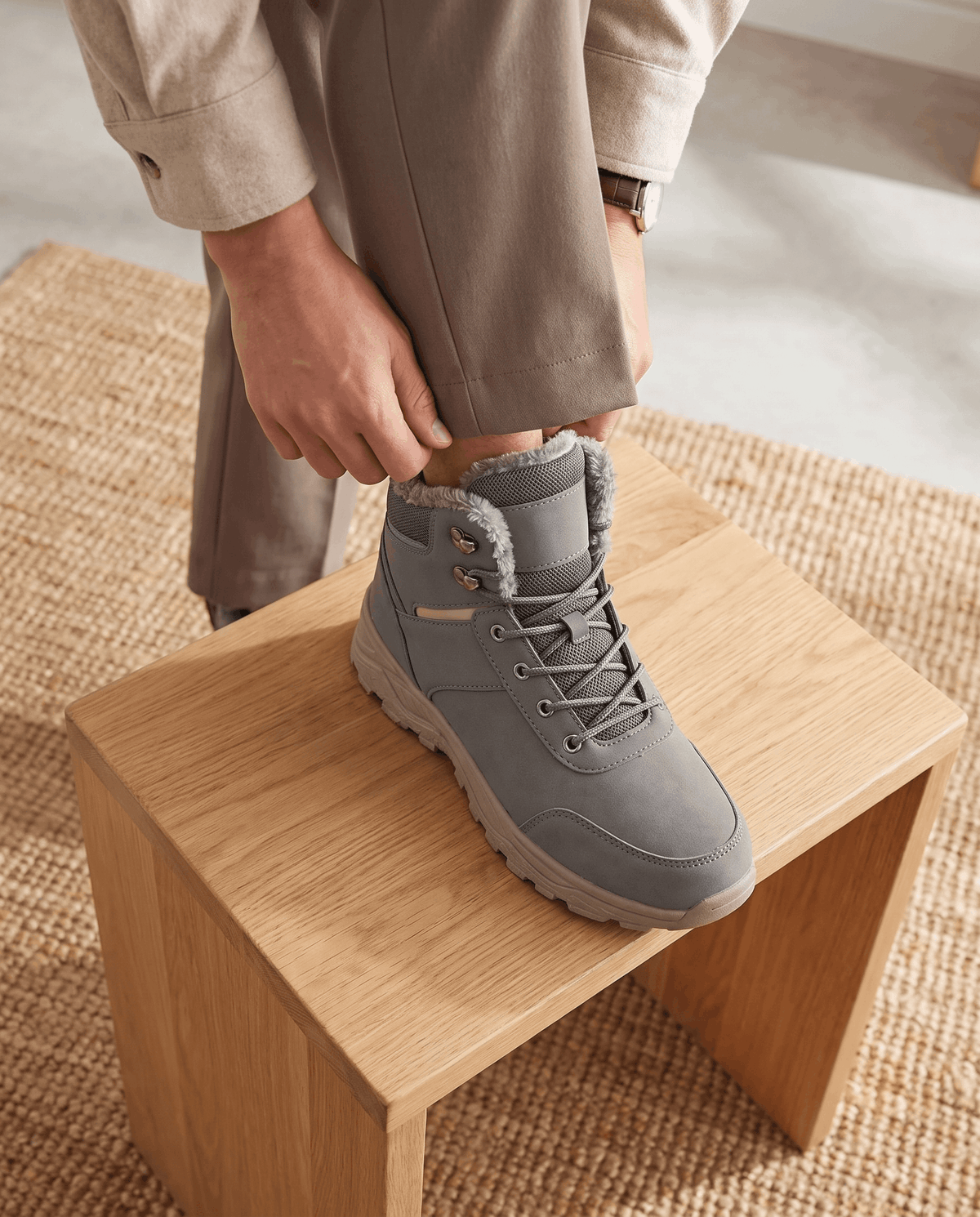 Person placing a gray winter boot on a wooden stool.