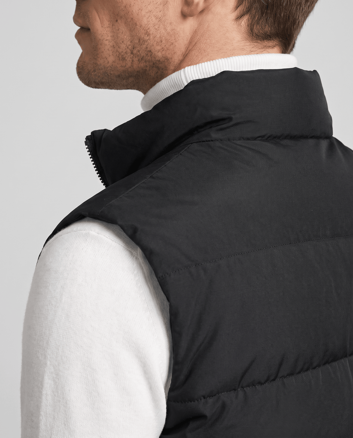 Side close-up of black quilted vest showing the high collar over a white sweater