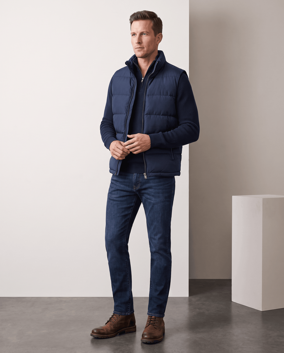 Man in navy quilted vest over a navy shirt with jeans and brown shoes in studio
