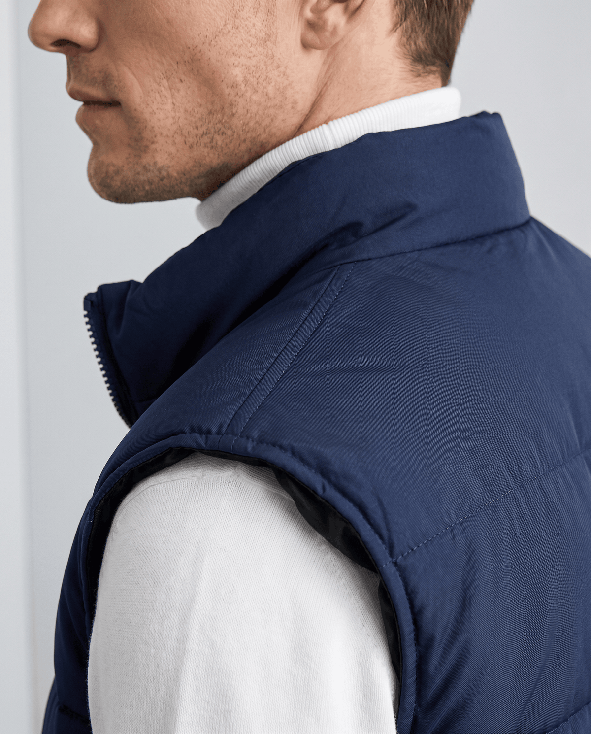 Side close-up of navy quilted vest showing the high collar over a white sweater