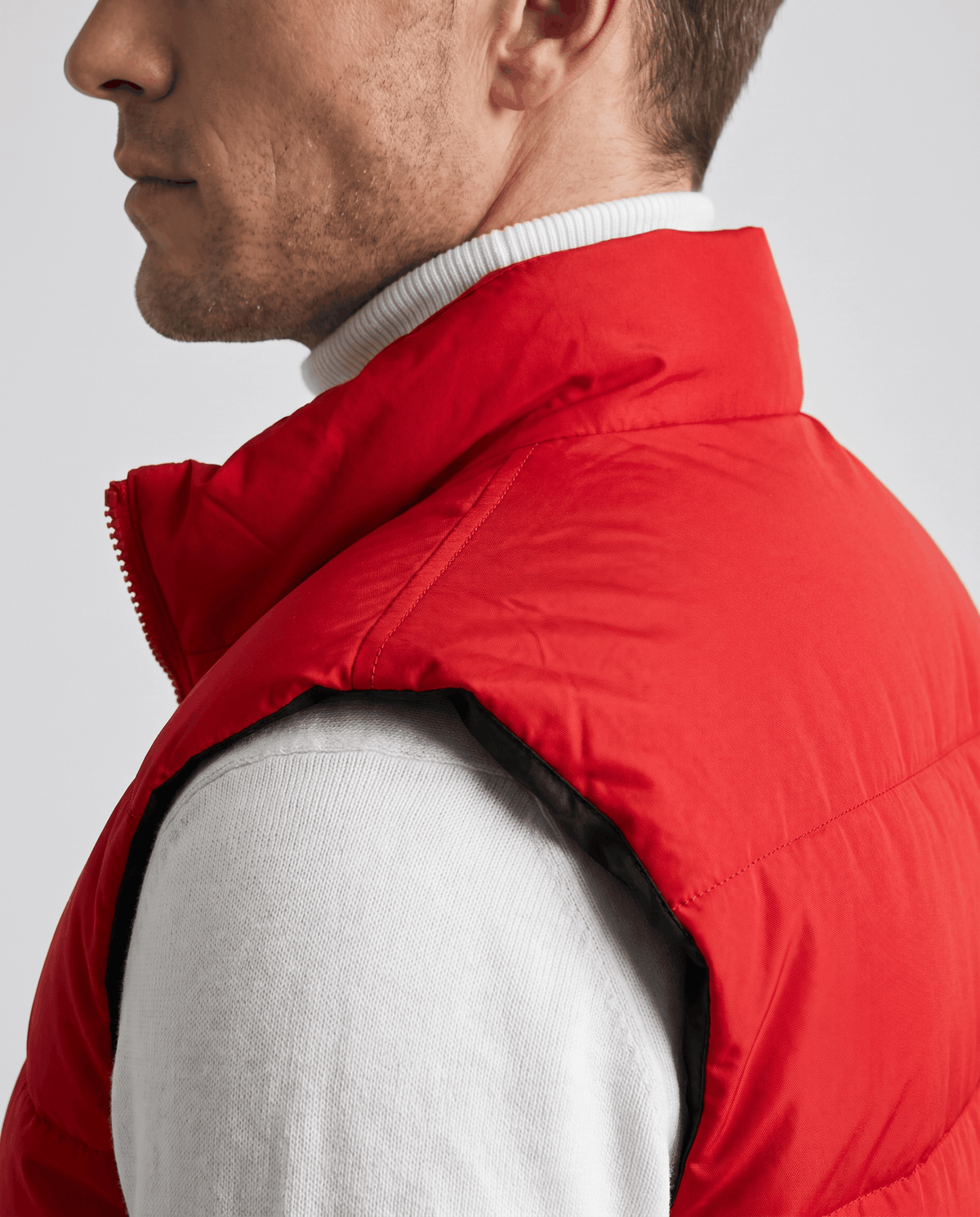 Side close-up of red quilted vest showing the high collar over a white sweater