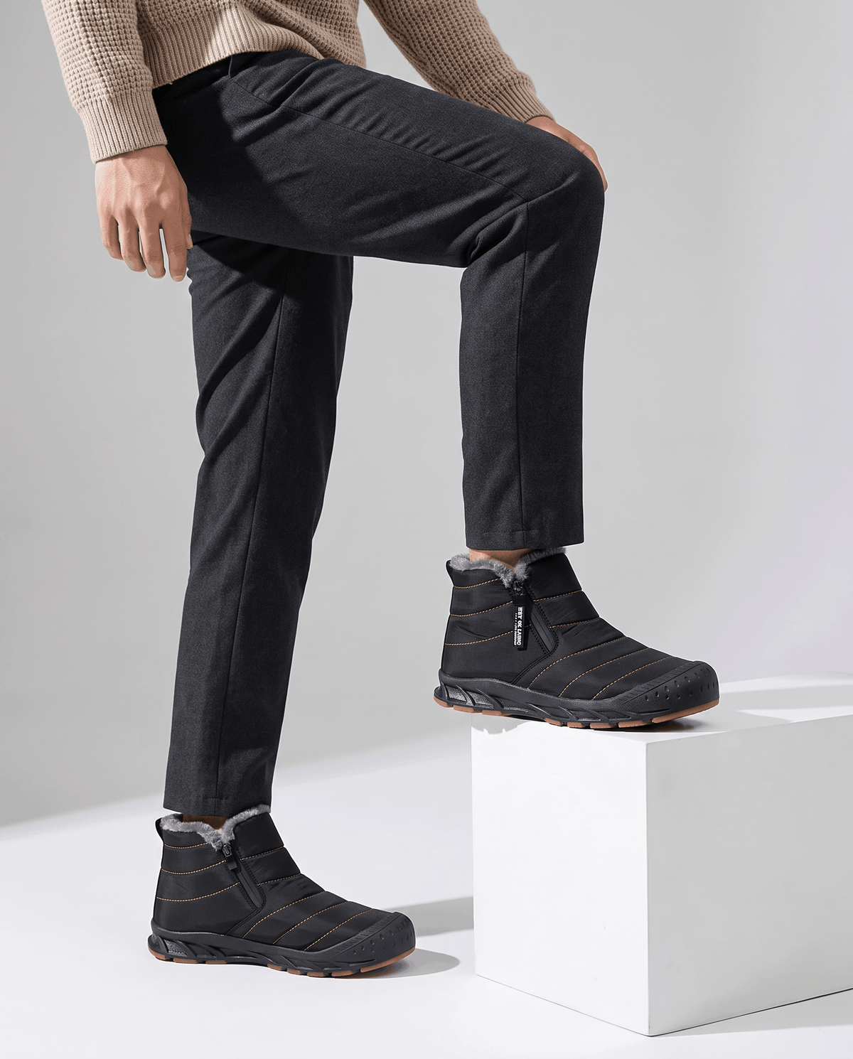 Person wearing black insulated boots while stepping onto a white pedestal.