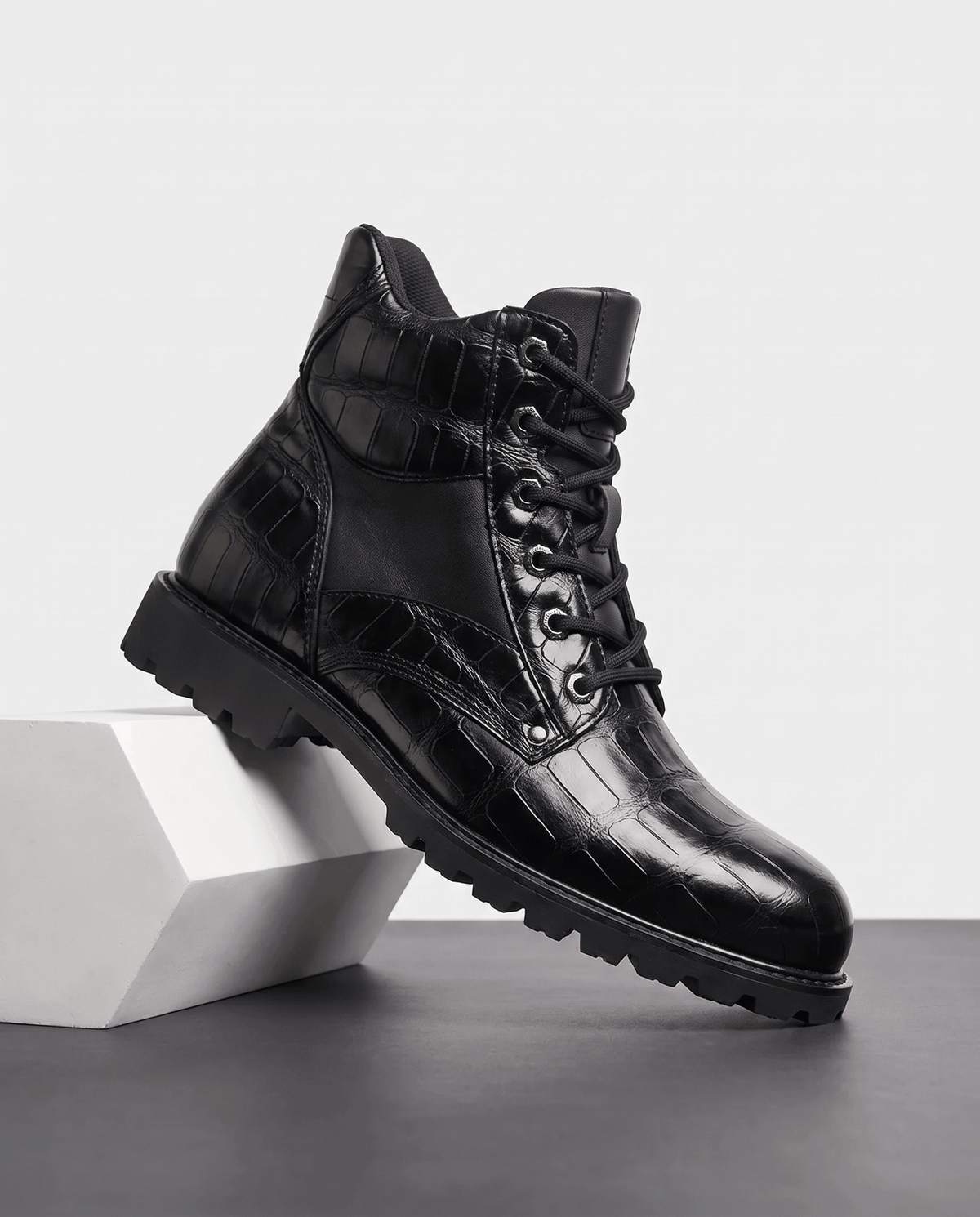 Black leather ankle boots with embossed reptile grain, polished metal eyelets, and a chunky lug outsole.