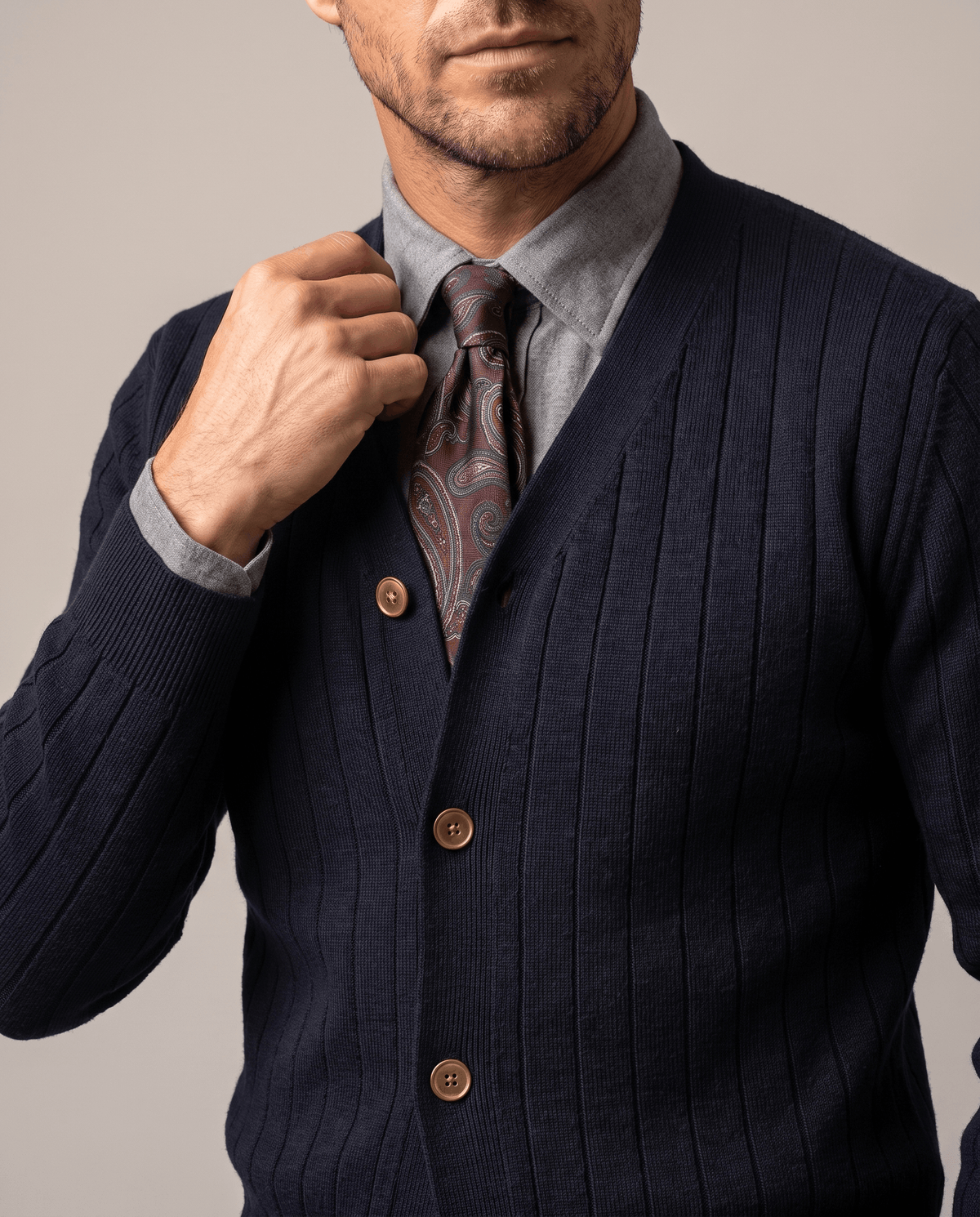 Hand at the V-neck of a navy cardigan worn over a blue shirt and brown tie