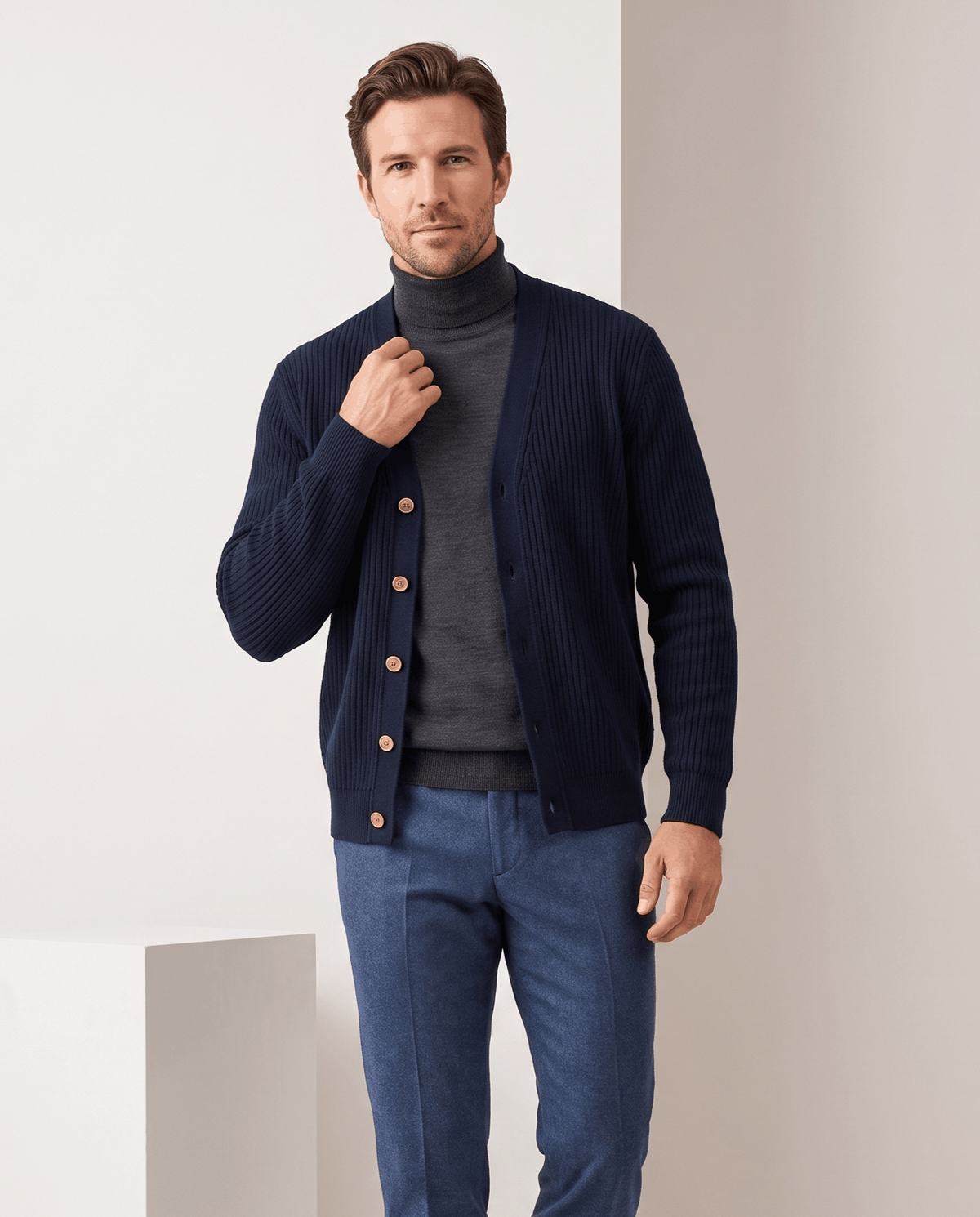 Navy ribbed cardigan with tan buttons worn over a charcoal turtleneck and blue trousers