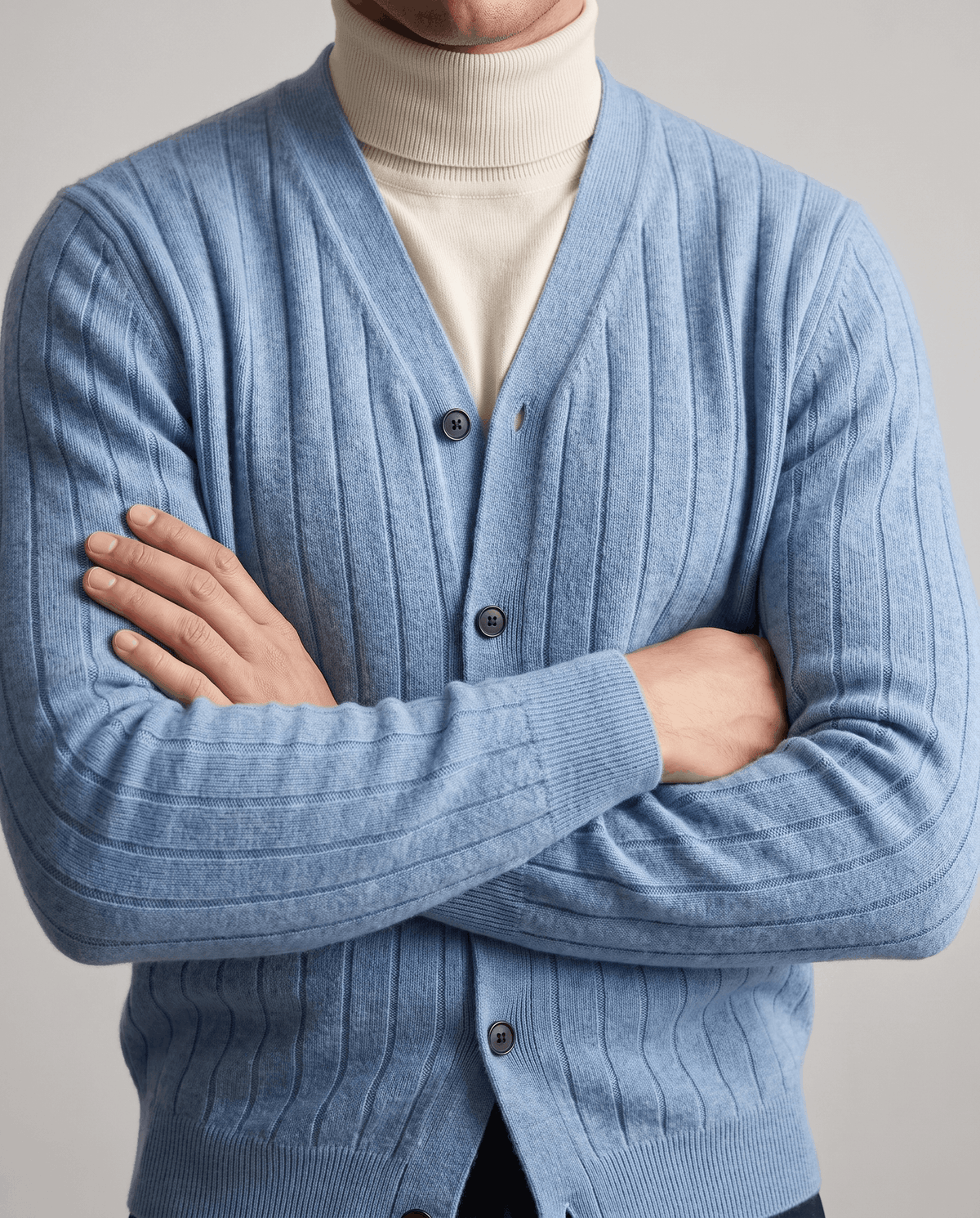 Arms crossed in a sky blue ribbed cardigan with navy buttons over a cream turtleneck