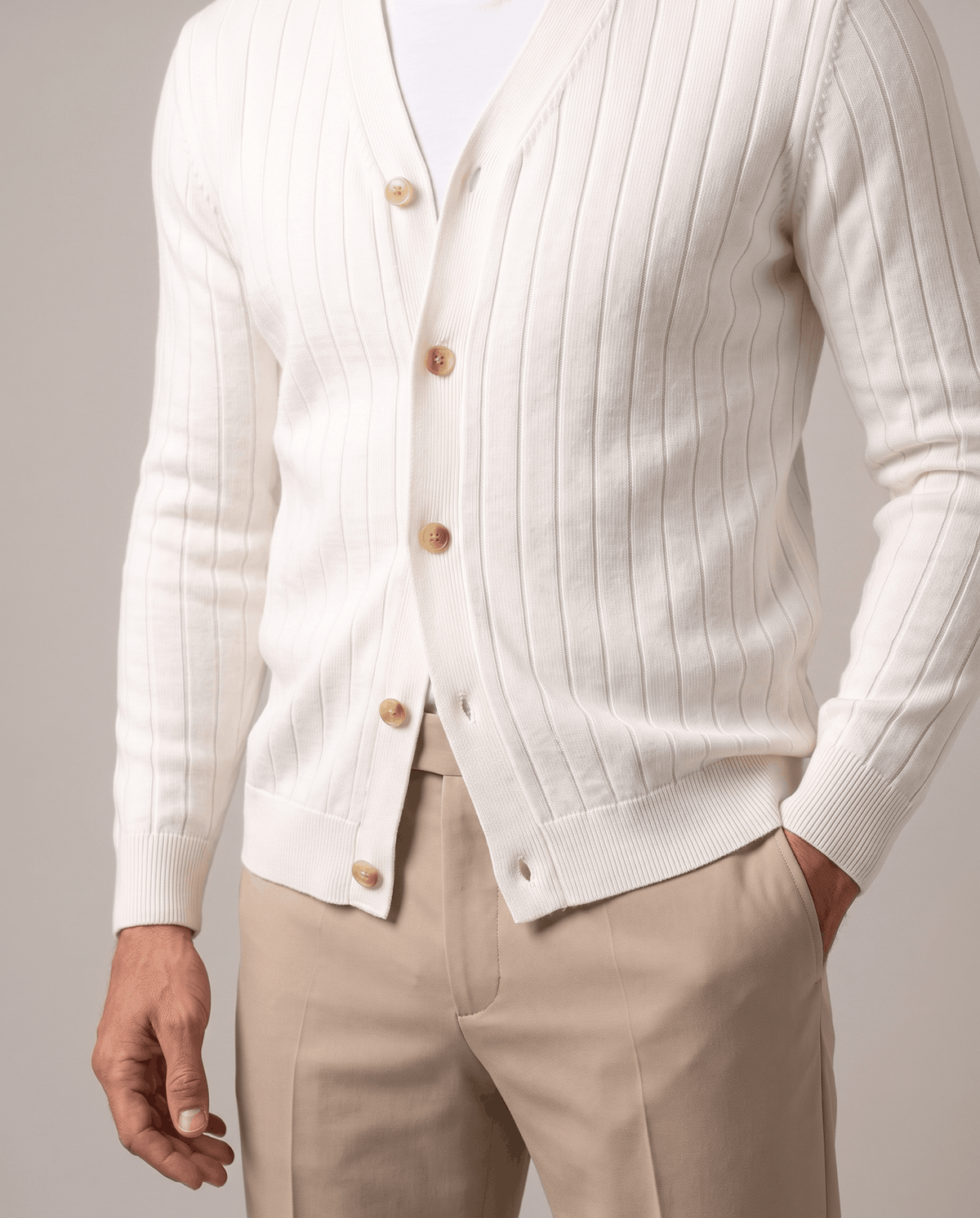 Close-up of the white cardigan buttoned with one hand in a khaki trouser pocket