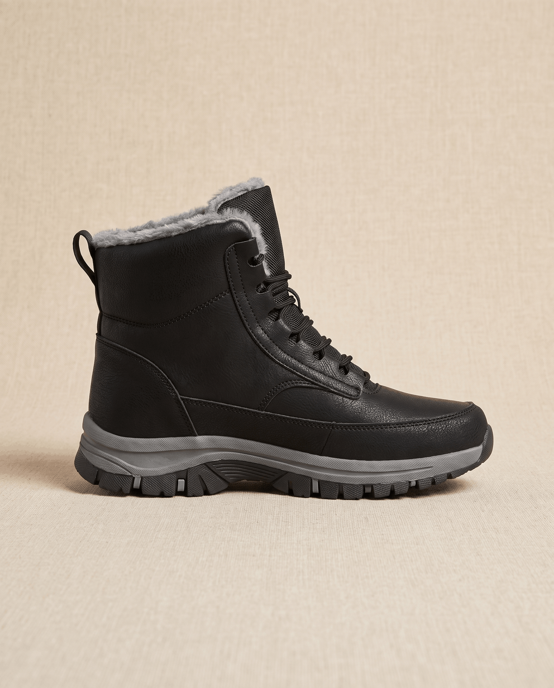 Black sherpa-lined lace-up winter boot shown from the side against a beige background.