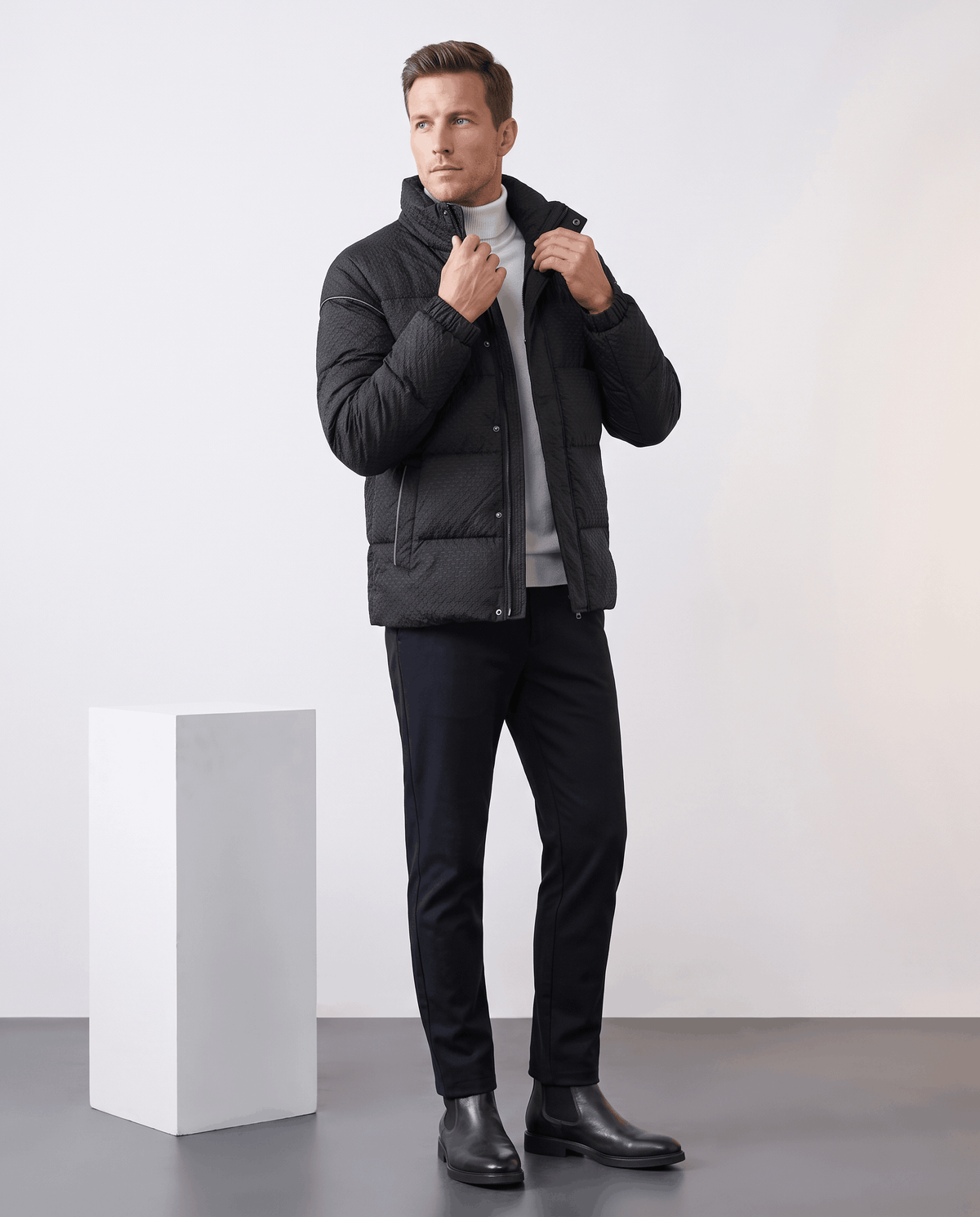 Full-length shot of a black puffer styled with dark trousers and Chelsea boots