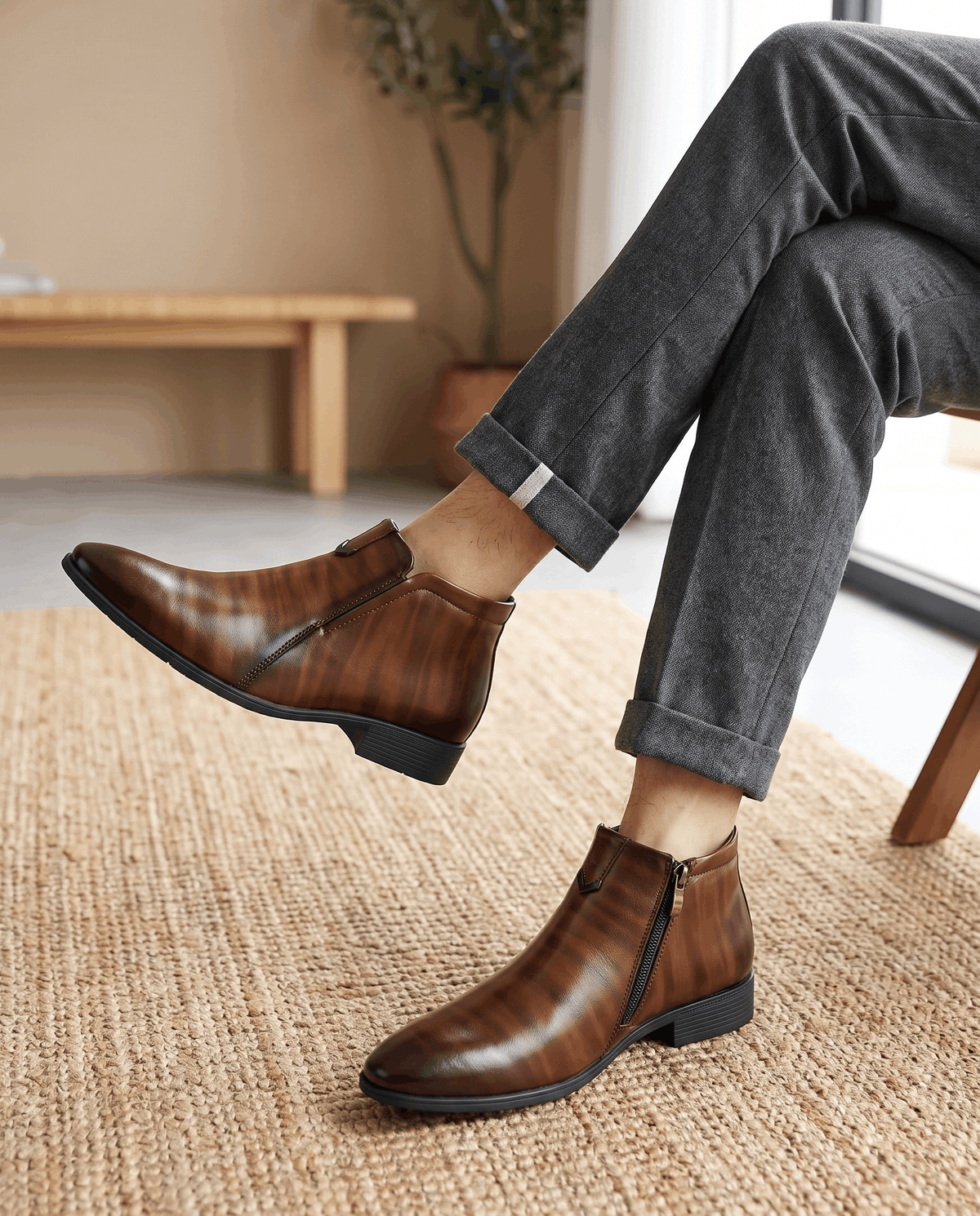 Polished brown grain leather side-zip ankle boots with a pointed toe, notched topline, and low block heel worn with grey trousers.