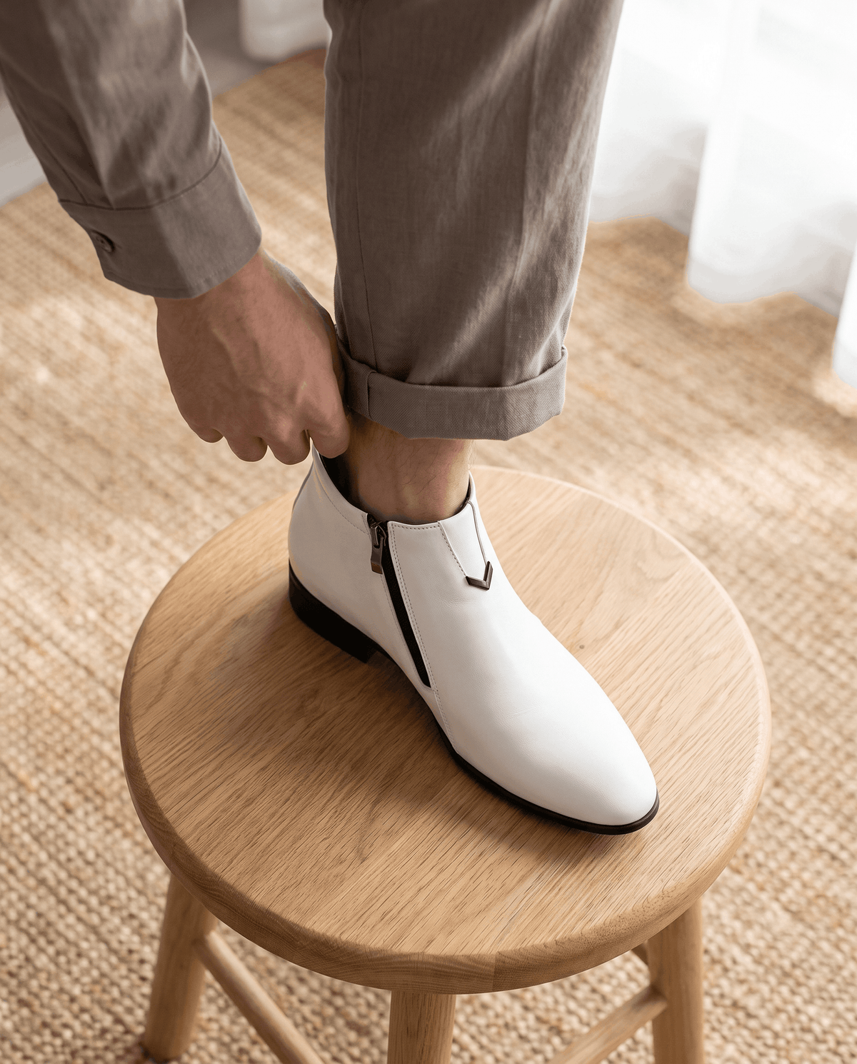 White polished grain side zip ankle boots with a pointed toe, notched topline, and black block heel on a wooden stool.