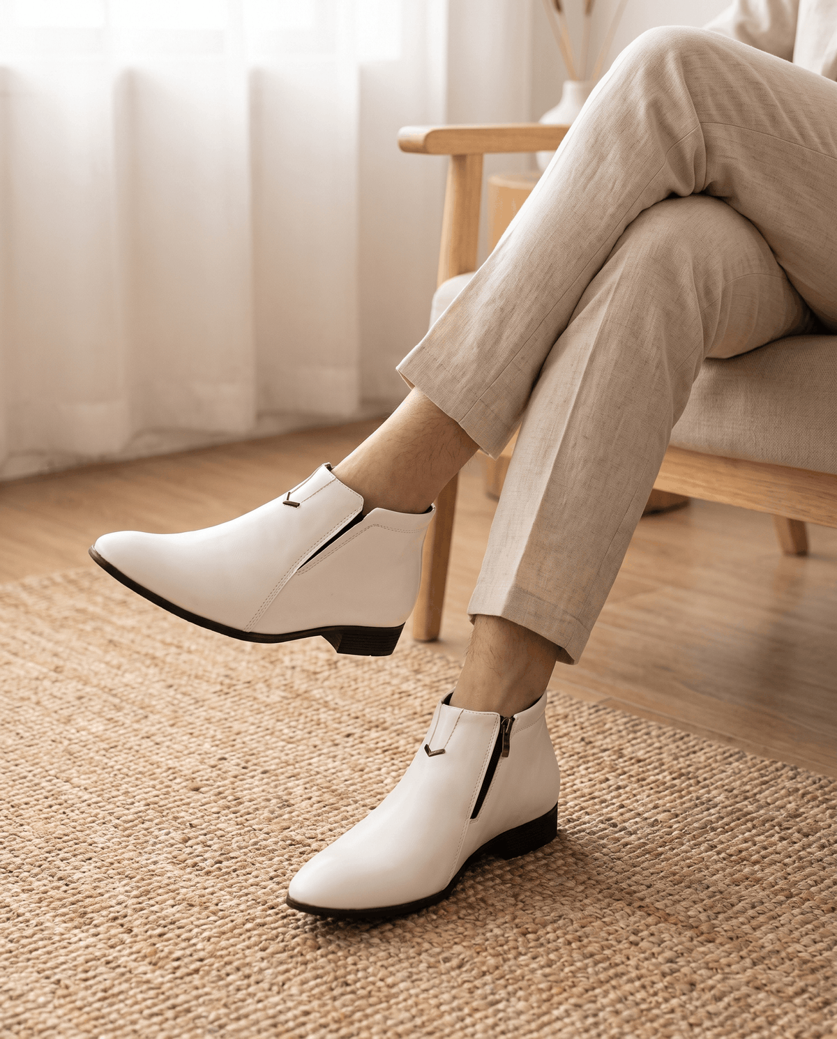White polished grain ankle boots with a pointed toe, side zip closure, and notched topline worn with beige trousers.
