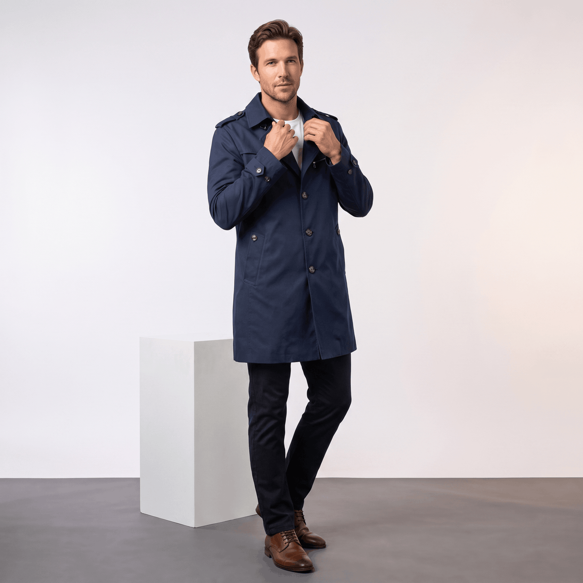 Man adjusting the front of a navy blue trench coat.