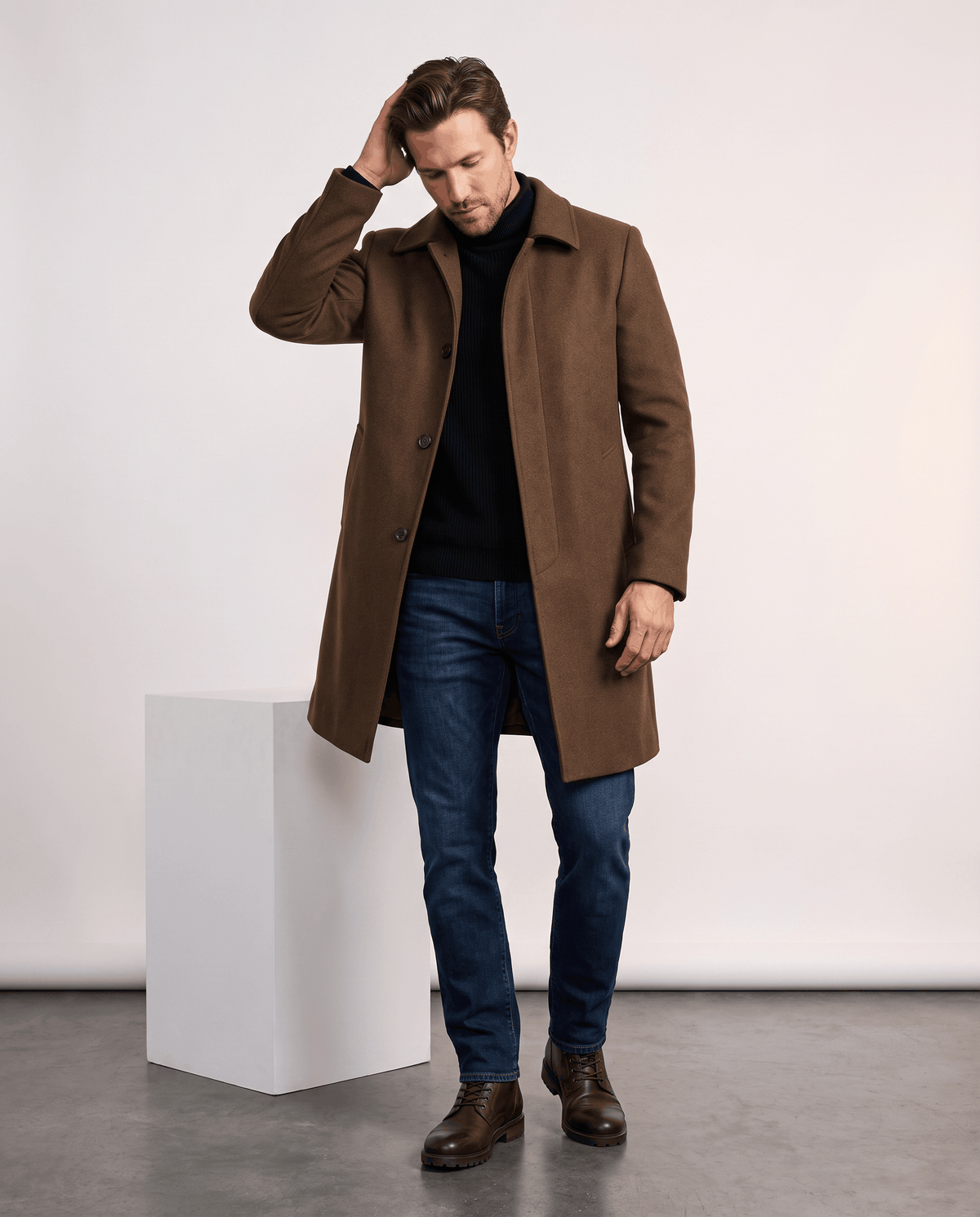 Brown wool overcoat in a side pose with one hand raised to the head