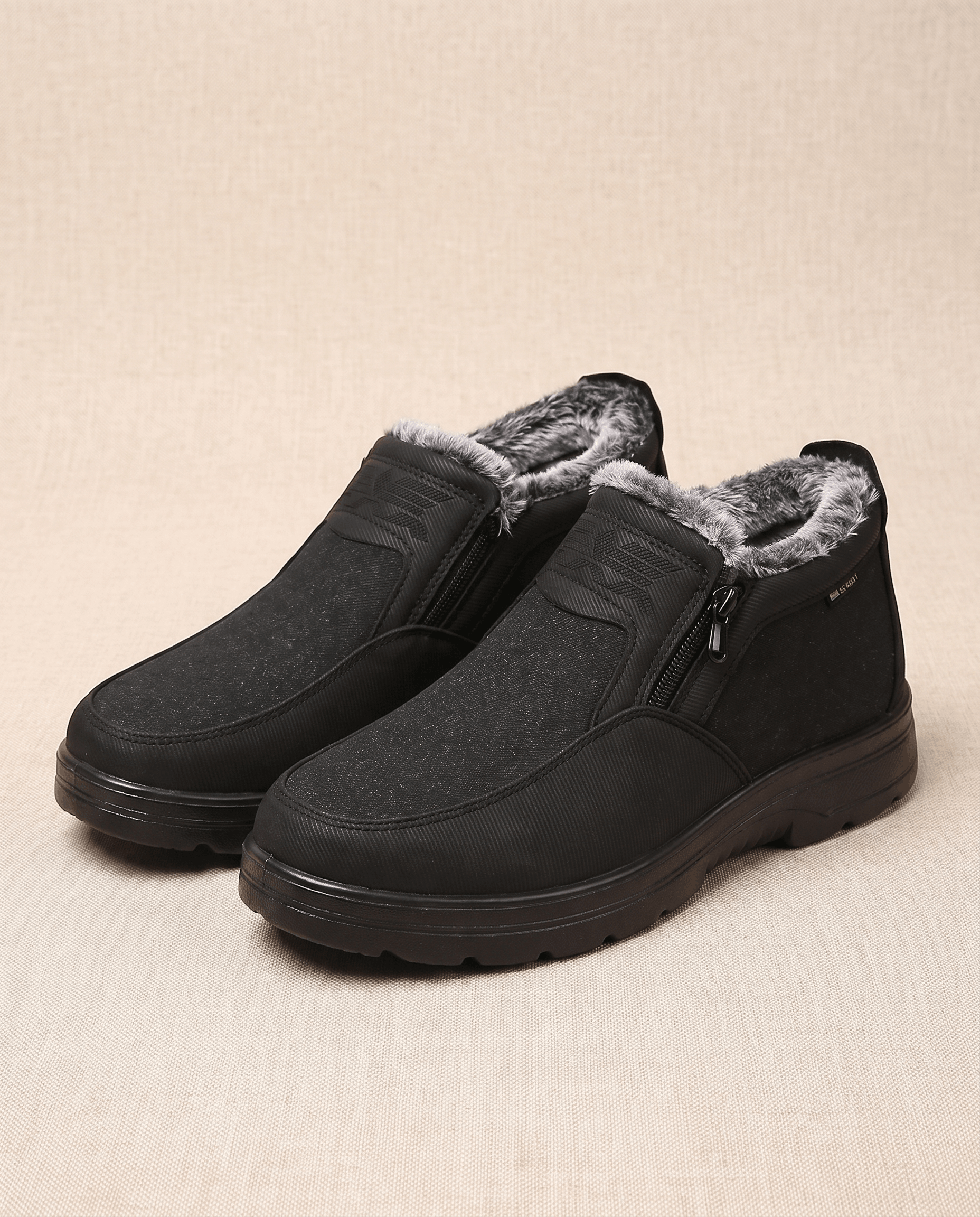 Black plush-lined slip-on ankle boots with side zips and rugged rubber soles displayed on a beige background.