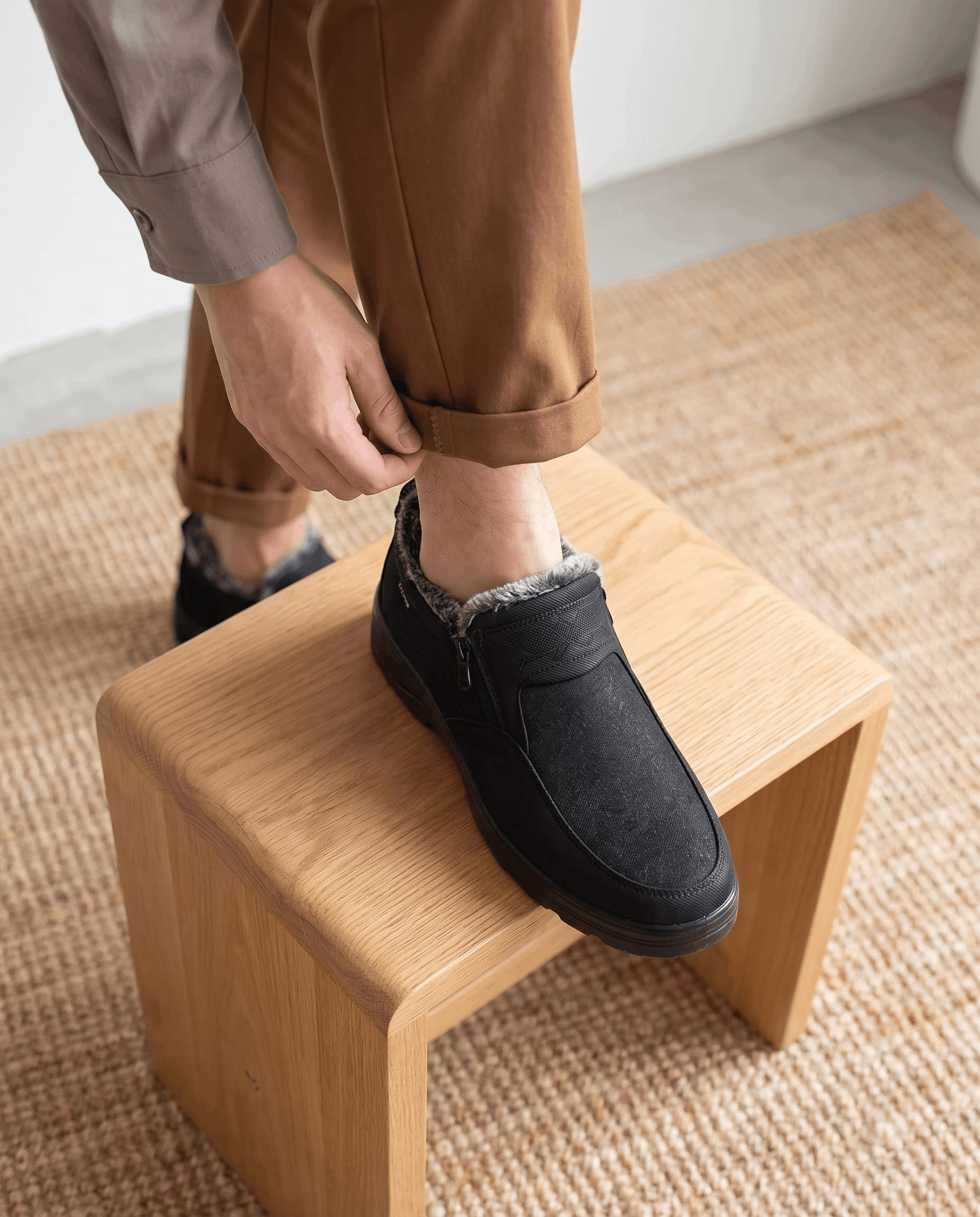 Person wearing a black fleece-lined ankle boot while standing on a wooden stool.