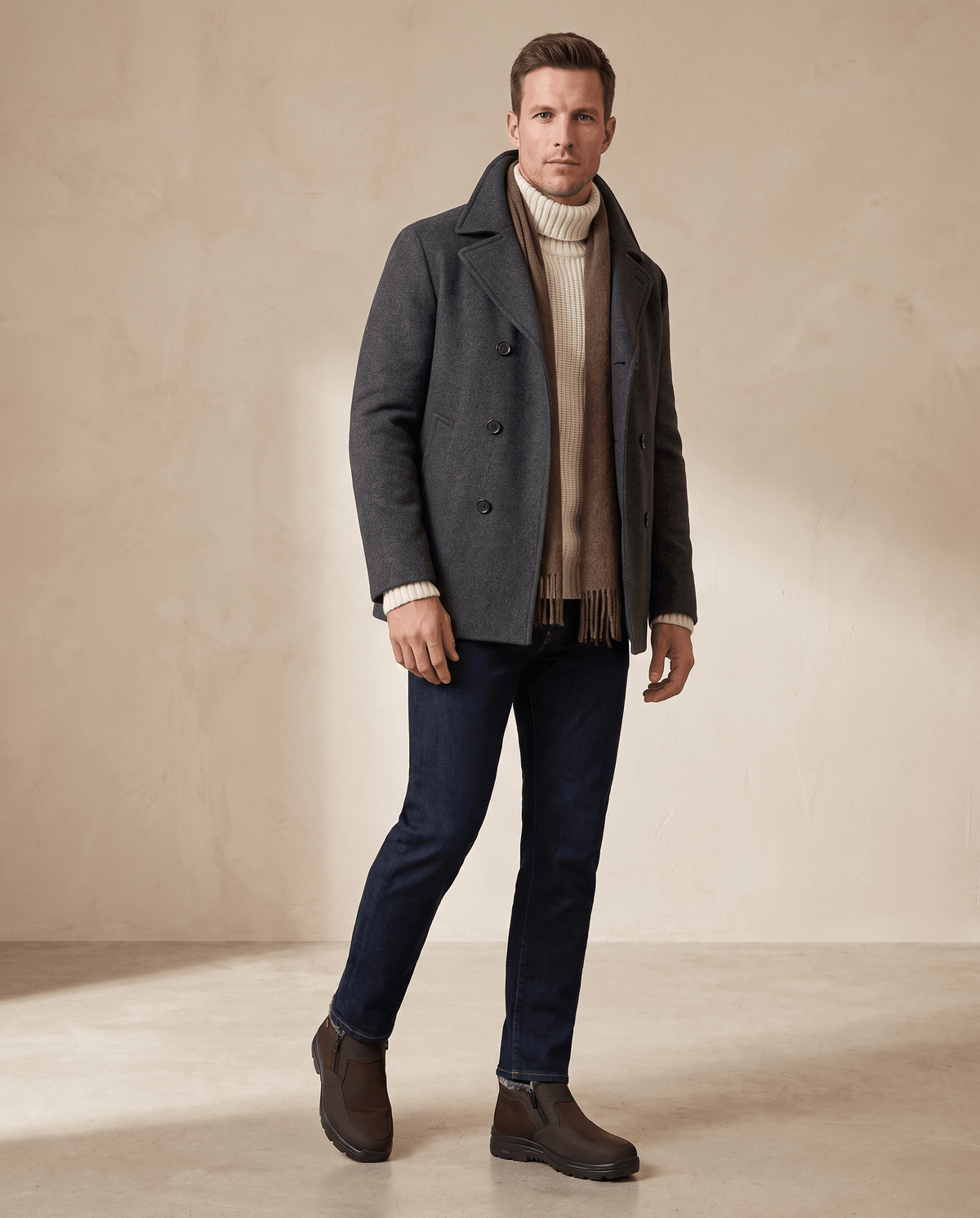 Man wearing brown ankle boots with a dark jacket and jeans in a minimalist setting.