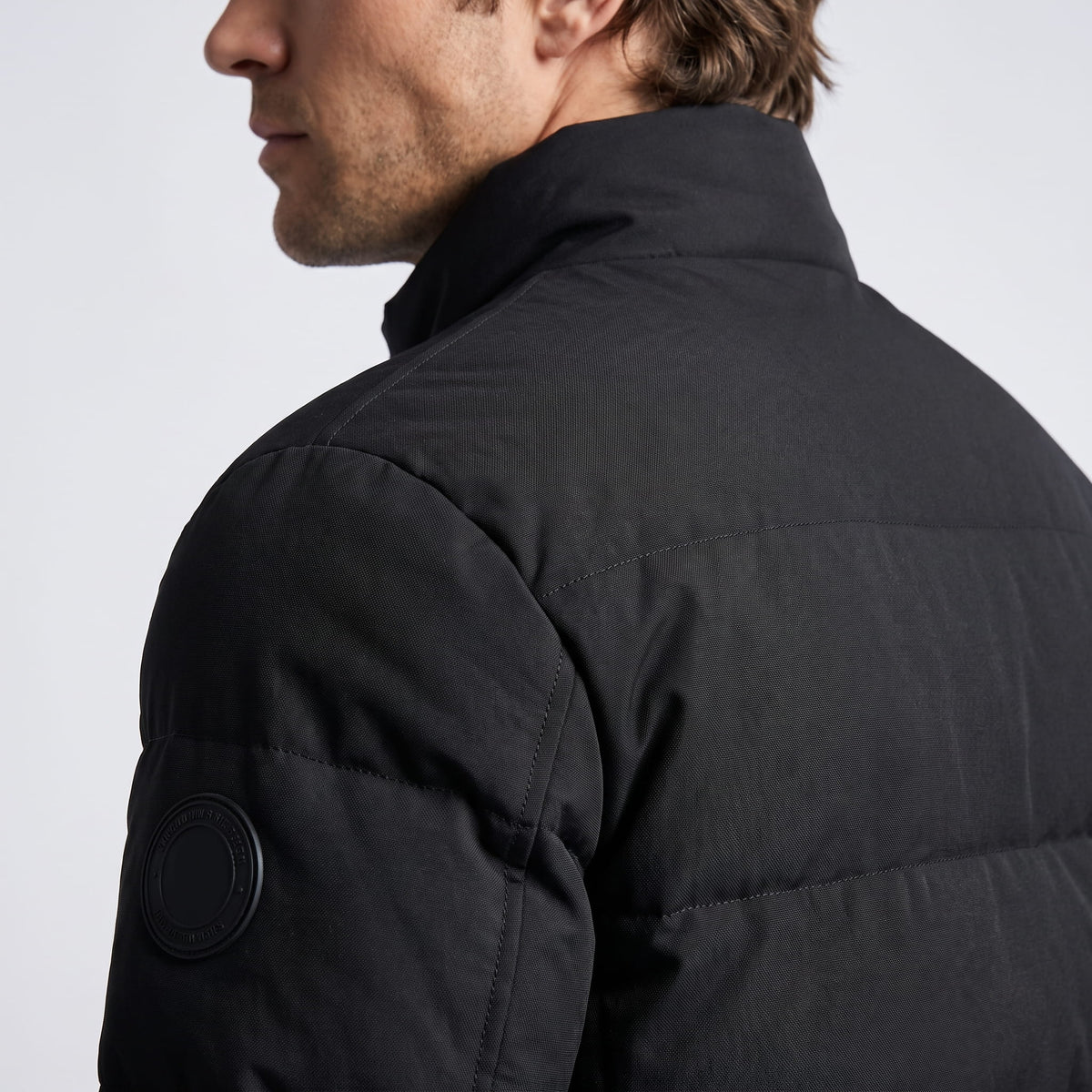 Black shoulder and upper-back detail showing the matte shell and sleeve patch