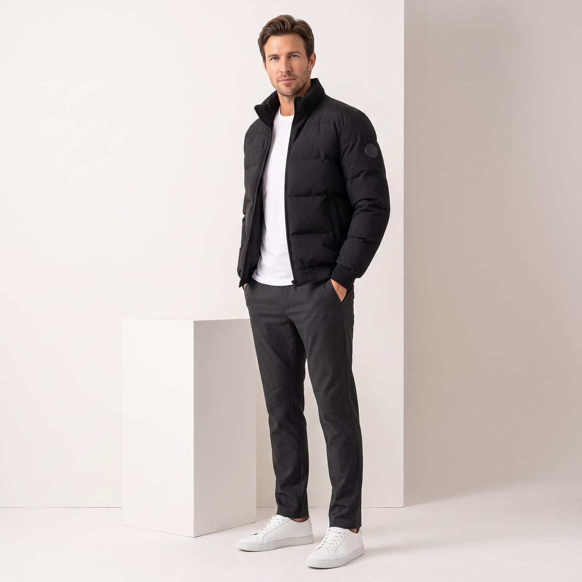 Black jacket styled with charcoal trousers and white sneakers, full-length view