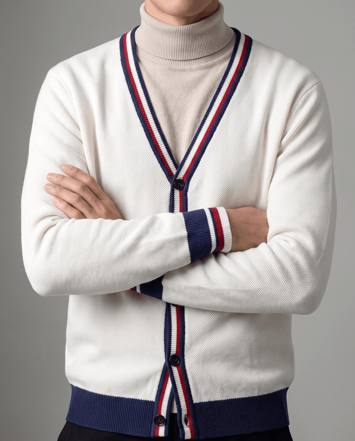 Arms crossed in a cream cardigan showing the navy, red and white striped placket