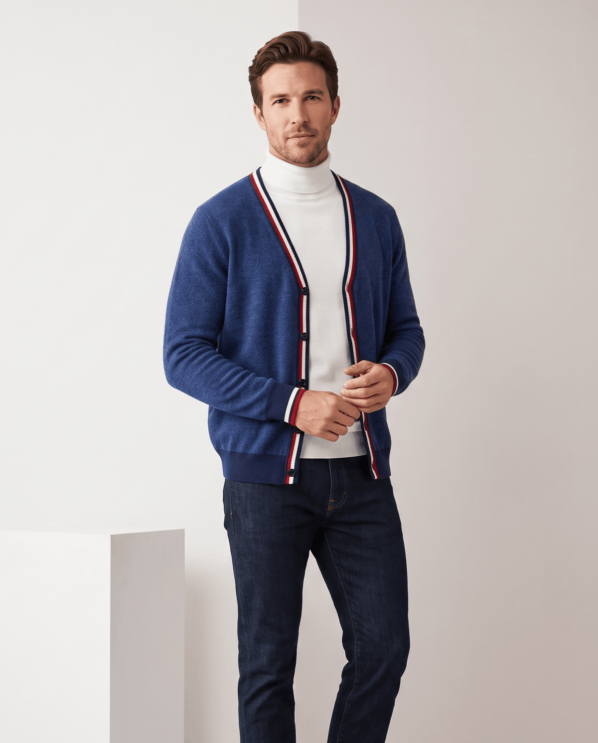 Man in a deep blue cardigan with striped trim over a white turtleneck and jeans